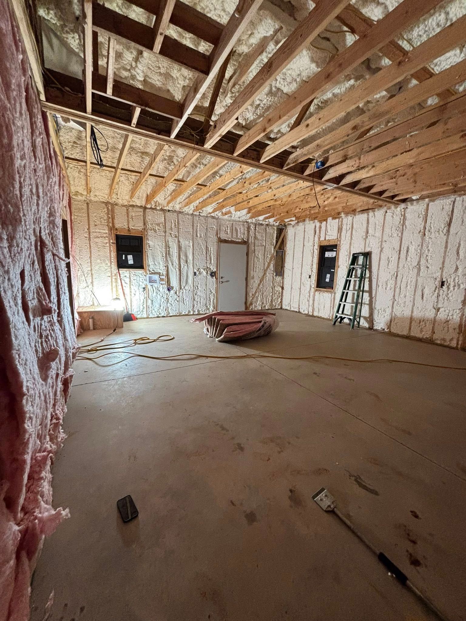 Unfinished room with exposed insulation, wooden rafters, and construction tools on the floor.