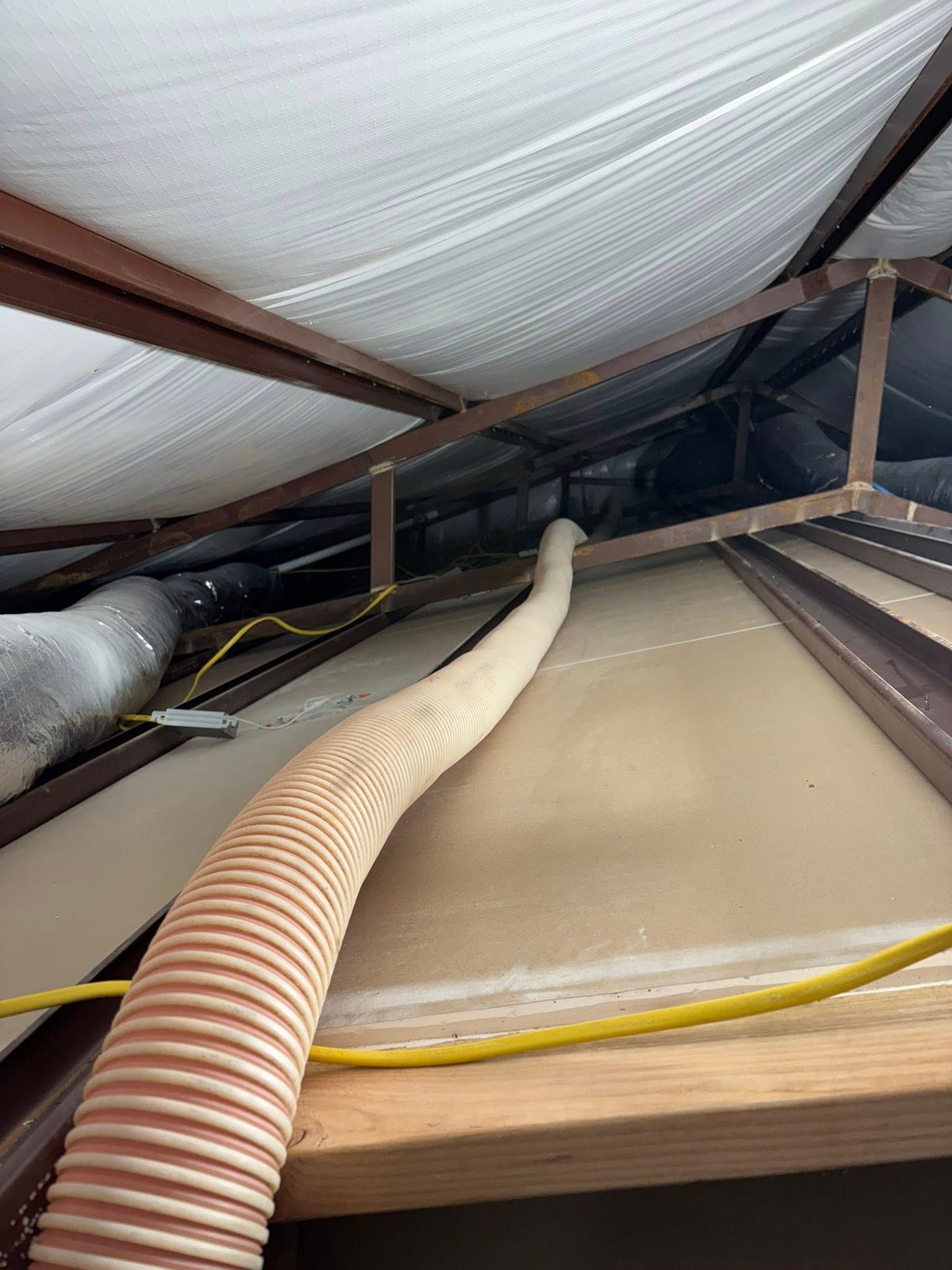 Close-up of attic insulation with hoses and wiring running under the roof rafters.
