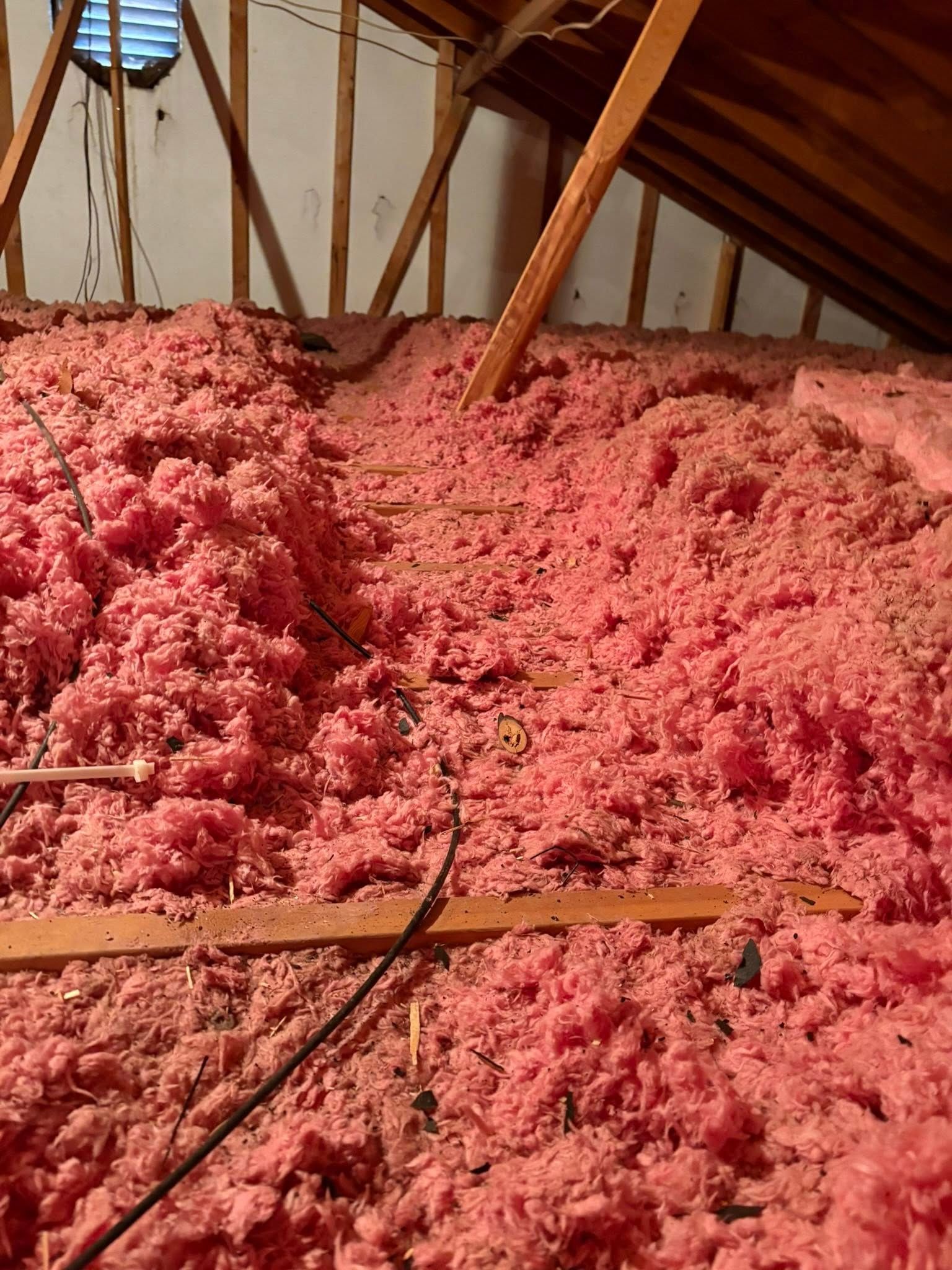 Attic filled with pink insulation batts and wooden rafters