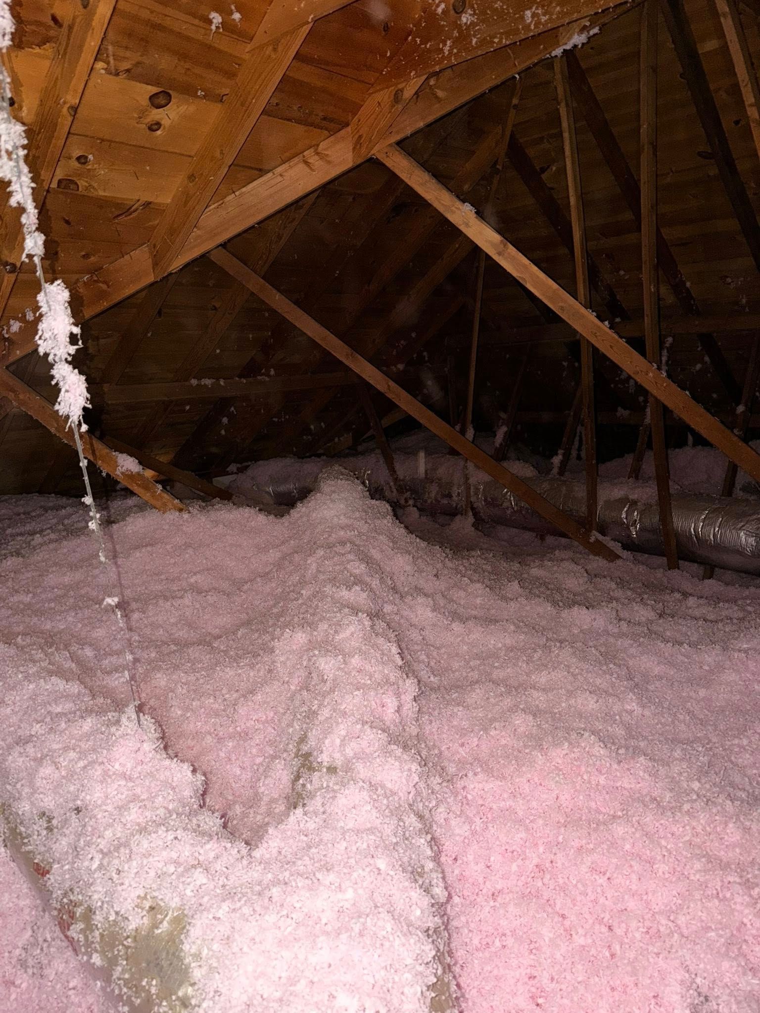 Insulated attic with exposed wooden rafters and a thick layer of pink fiberglass insulation on the floor
