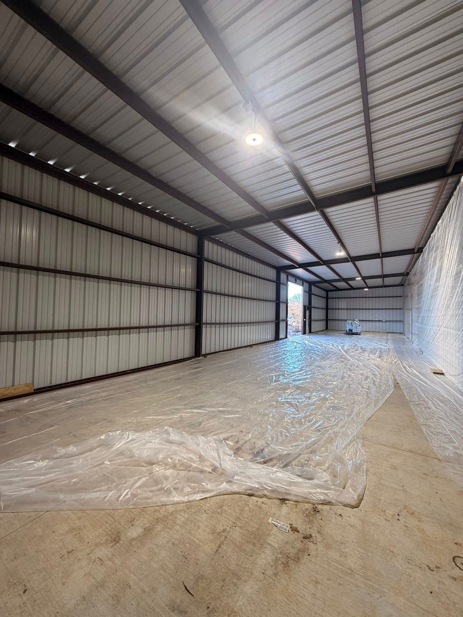 Interior of a metal warehouse with a dirt floor, plastic sheeting, and exposed beams under bright lights