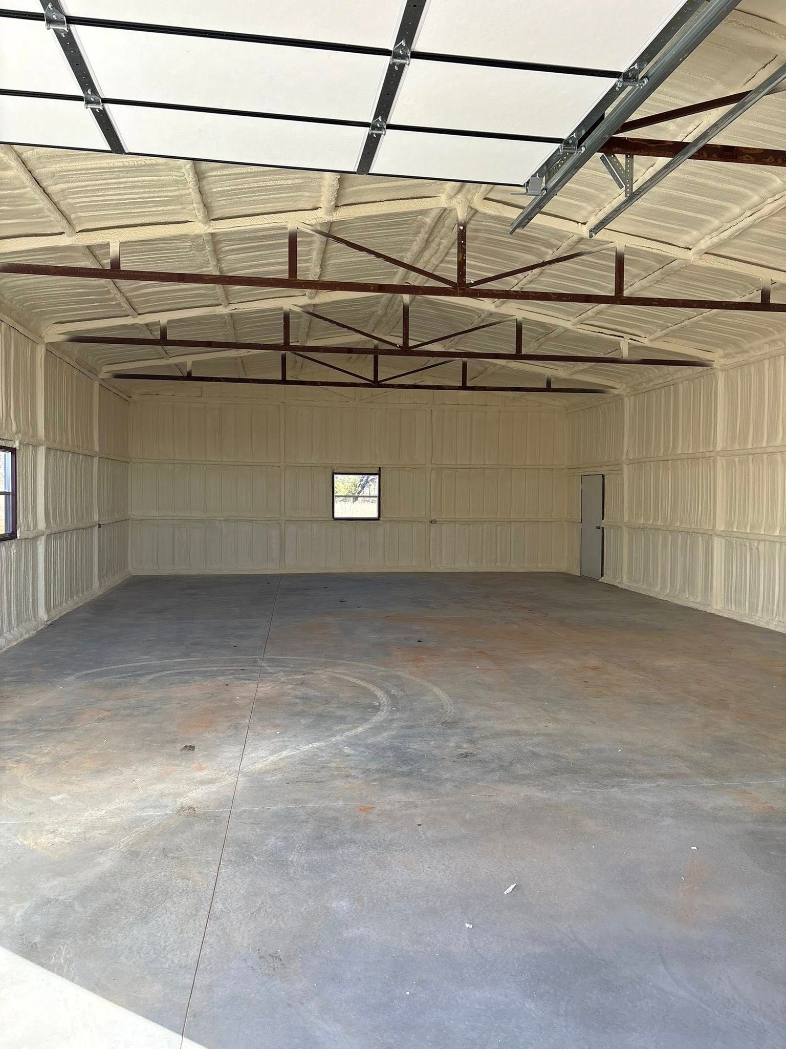 Empty insulated garage interior with concrete floor and open ceiling framing