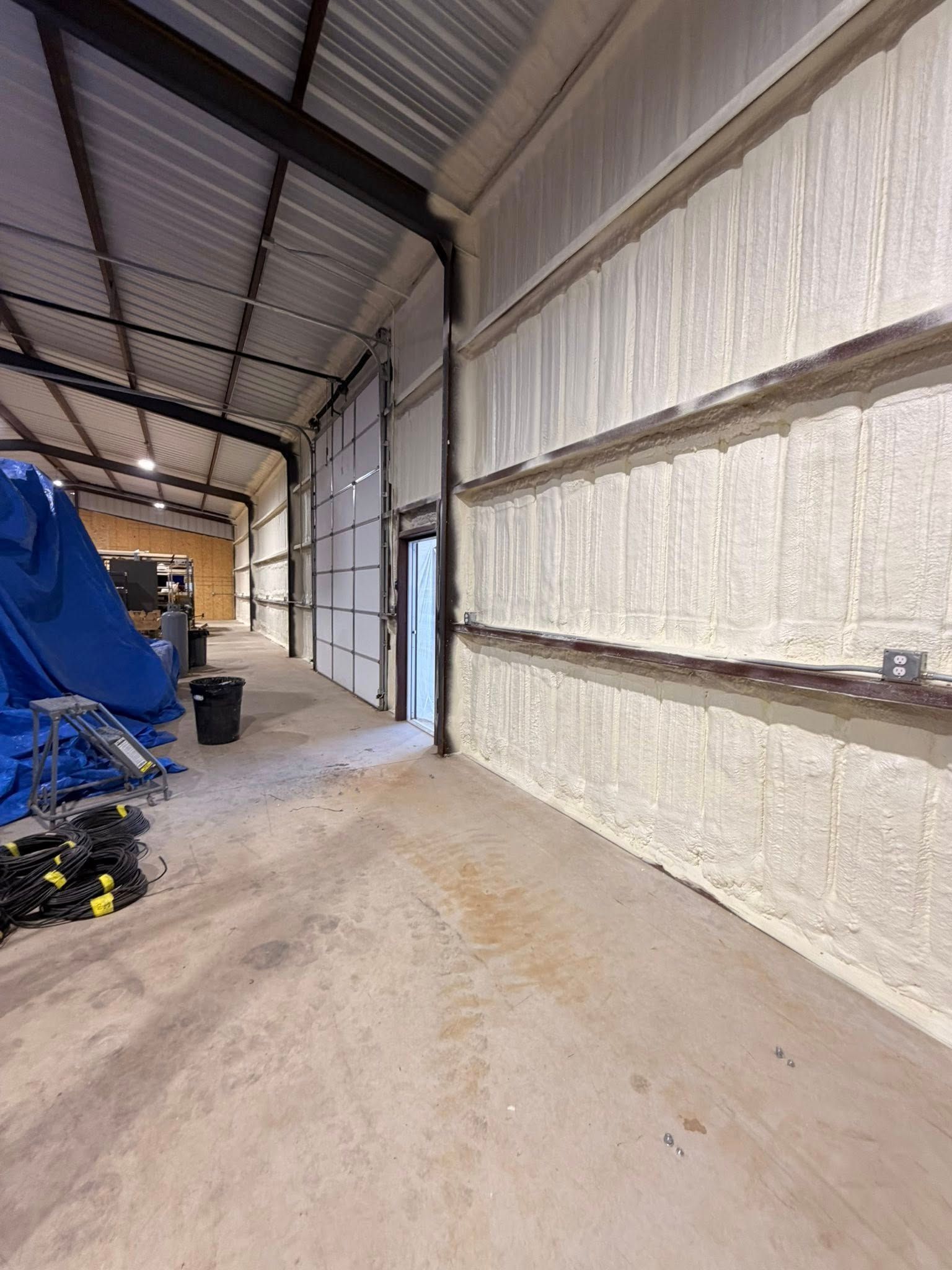 Interior of a warehouse with insulated walls, a concrete floor, and stacked equipment along the left side.