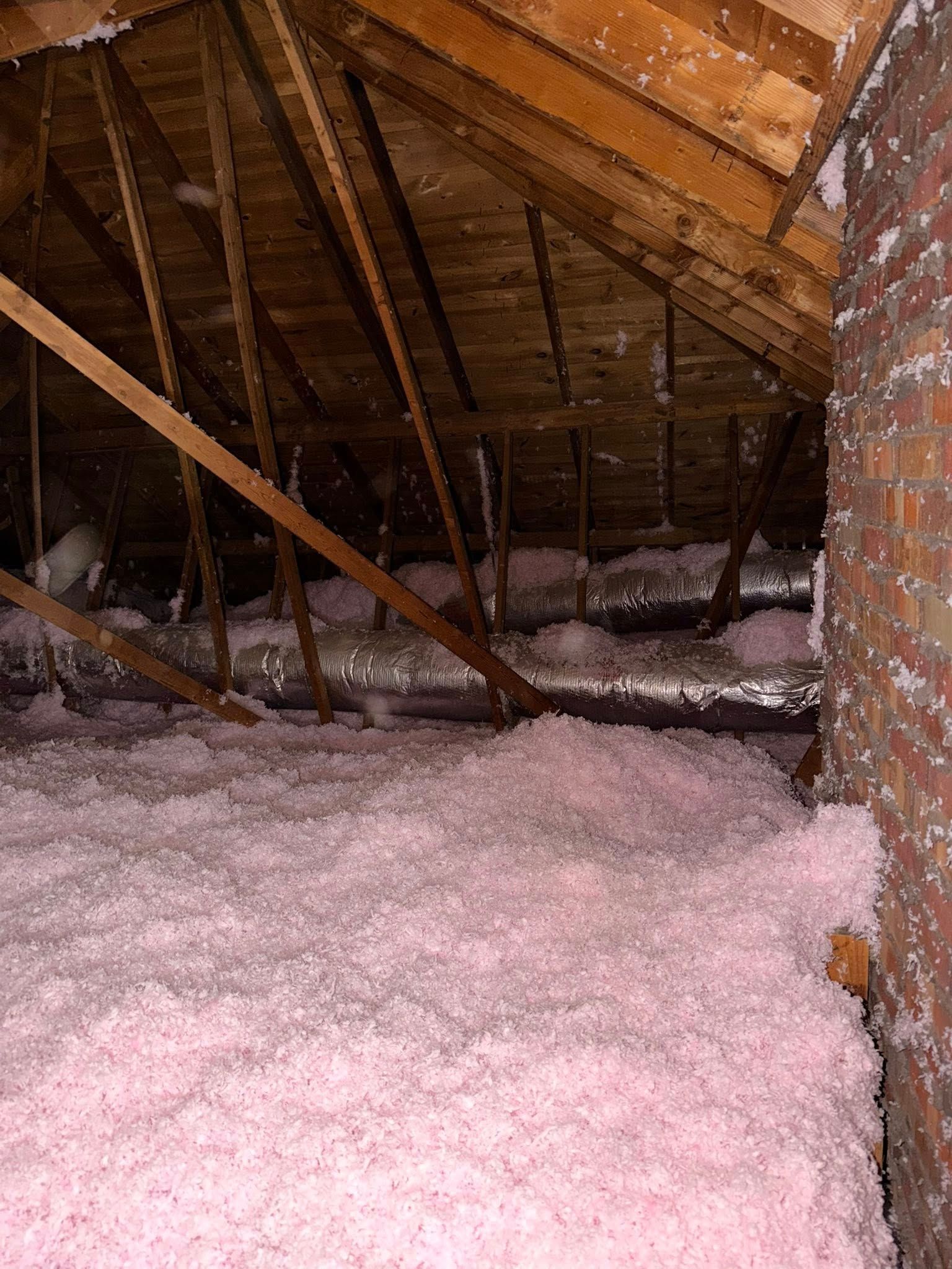 Snow-covered attic with exposed wooden rafters and insulation around a brick chimney opening