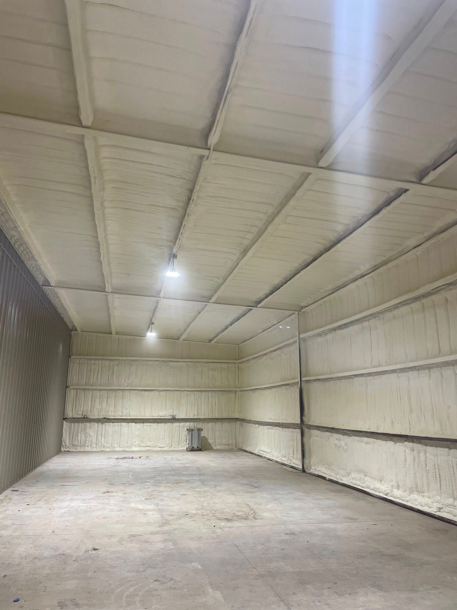 Empty industrial storage room with white insulated walls, concrete floor, and hanging lights