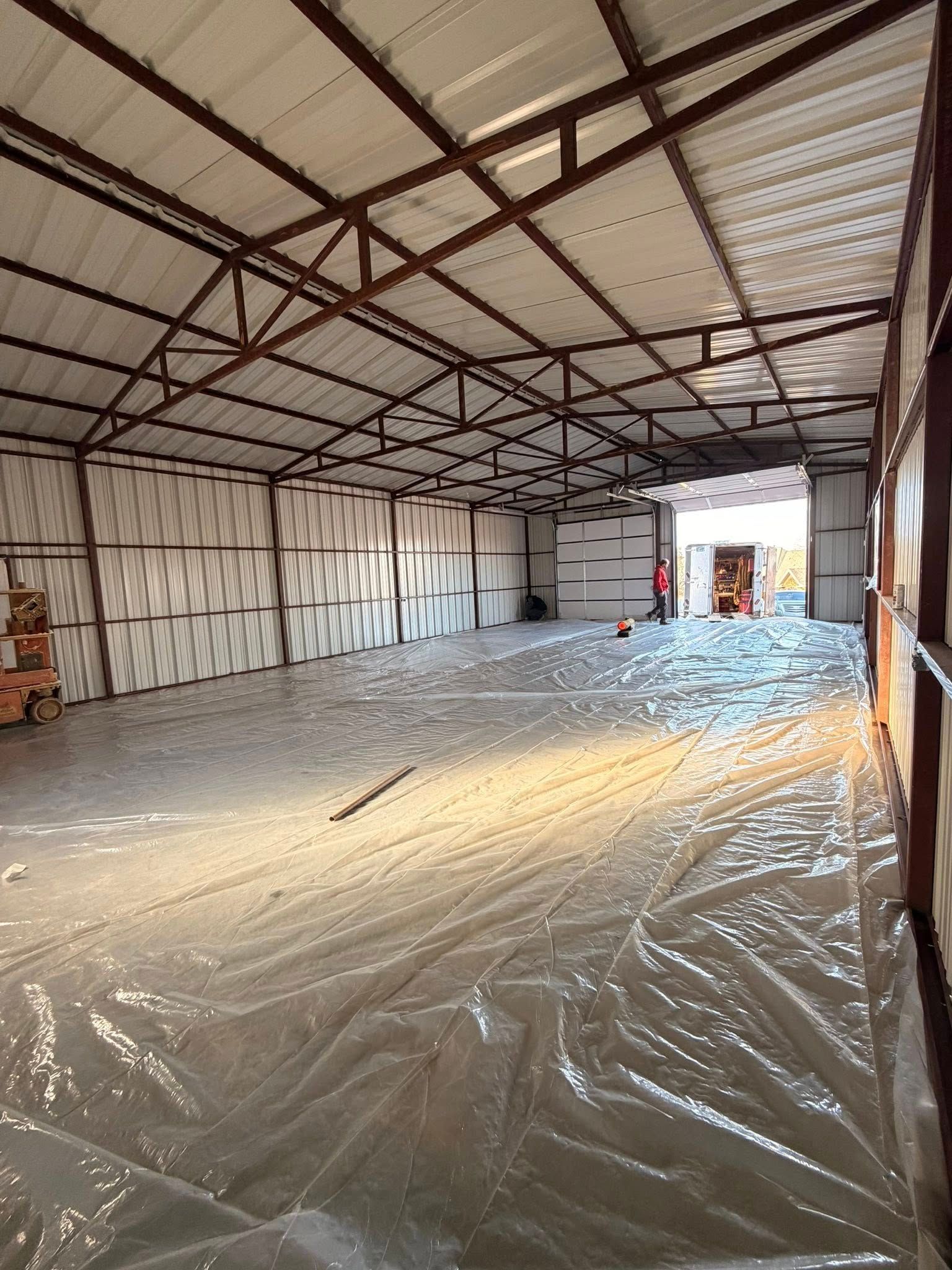 Empty warehouse interior with metal roof trusses and plastic sheeting covering the floor