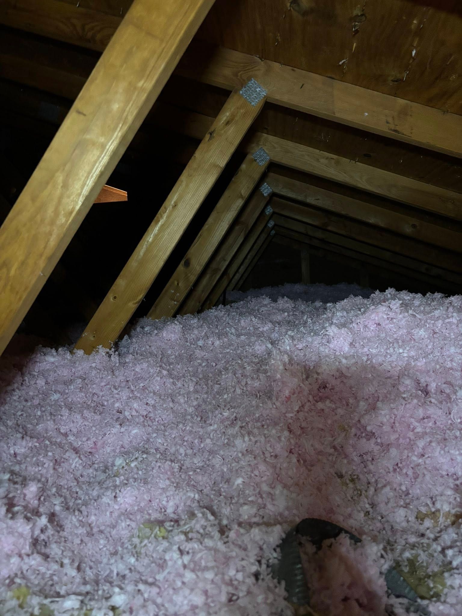Attic with wooden beams and a large mound of pink insulation around a vent opening