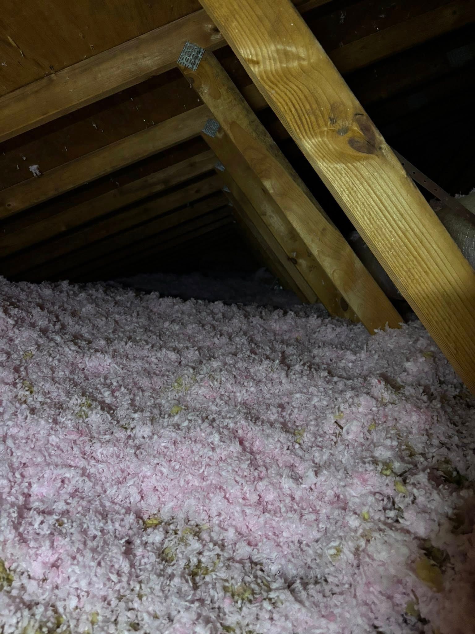 Attic with exposed wooden beams and pink-white insulation filling the floor area