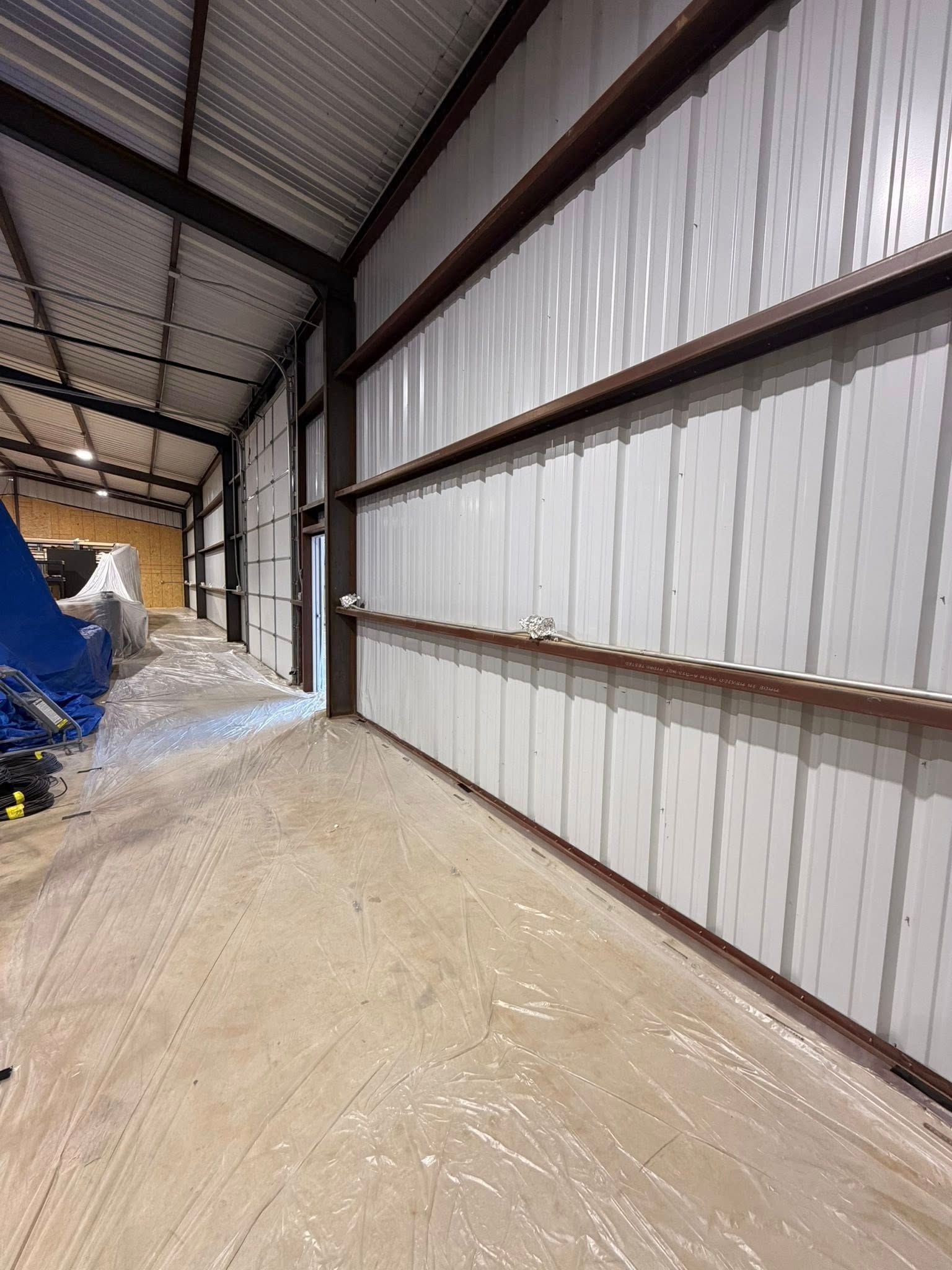 Empty metal warehouse interior with corrugated walls, exposed beams, and a covered dirt floor