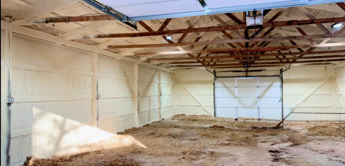 Empty barn interior with white walls, exposed roof trusses, and a dirt floor.