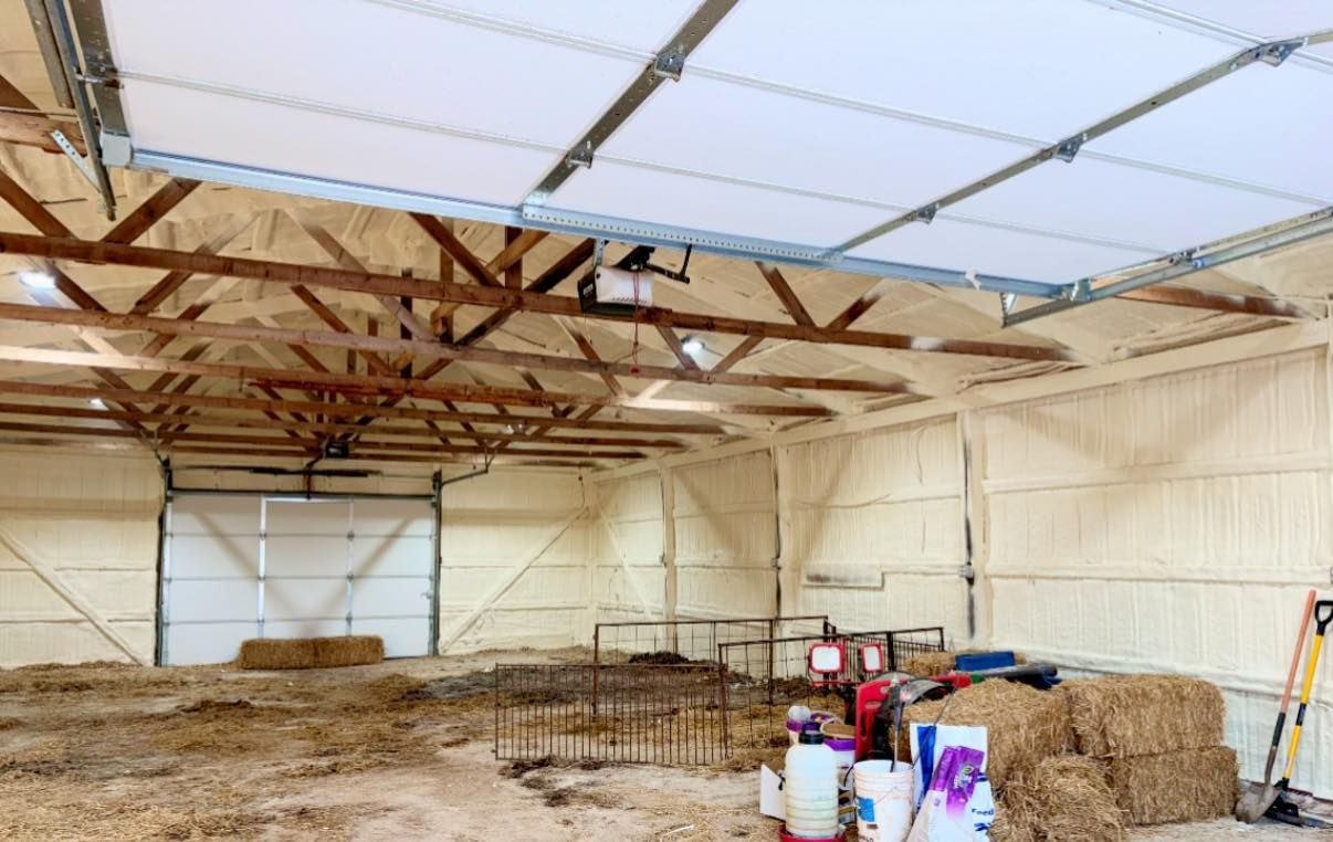 Large empty barn interior with hay bales, tools, and a metal truss roof under translucent panels