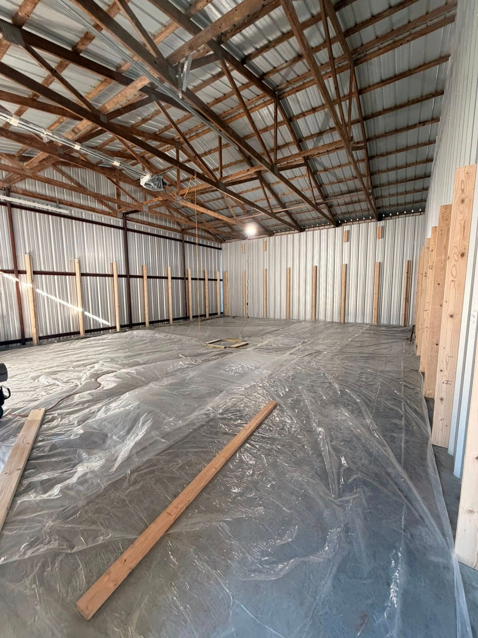 Empty unfinished warehouse interior with metal roof trusses, bare walls, and debris on the floor