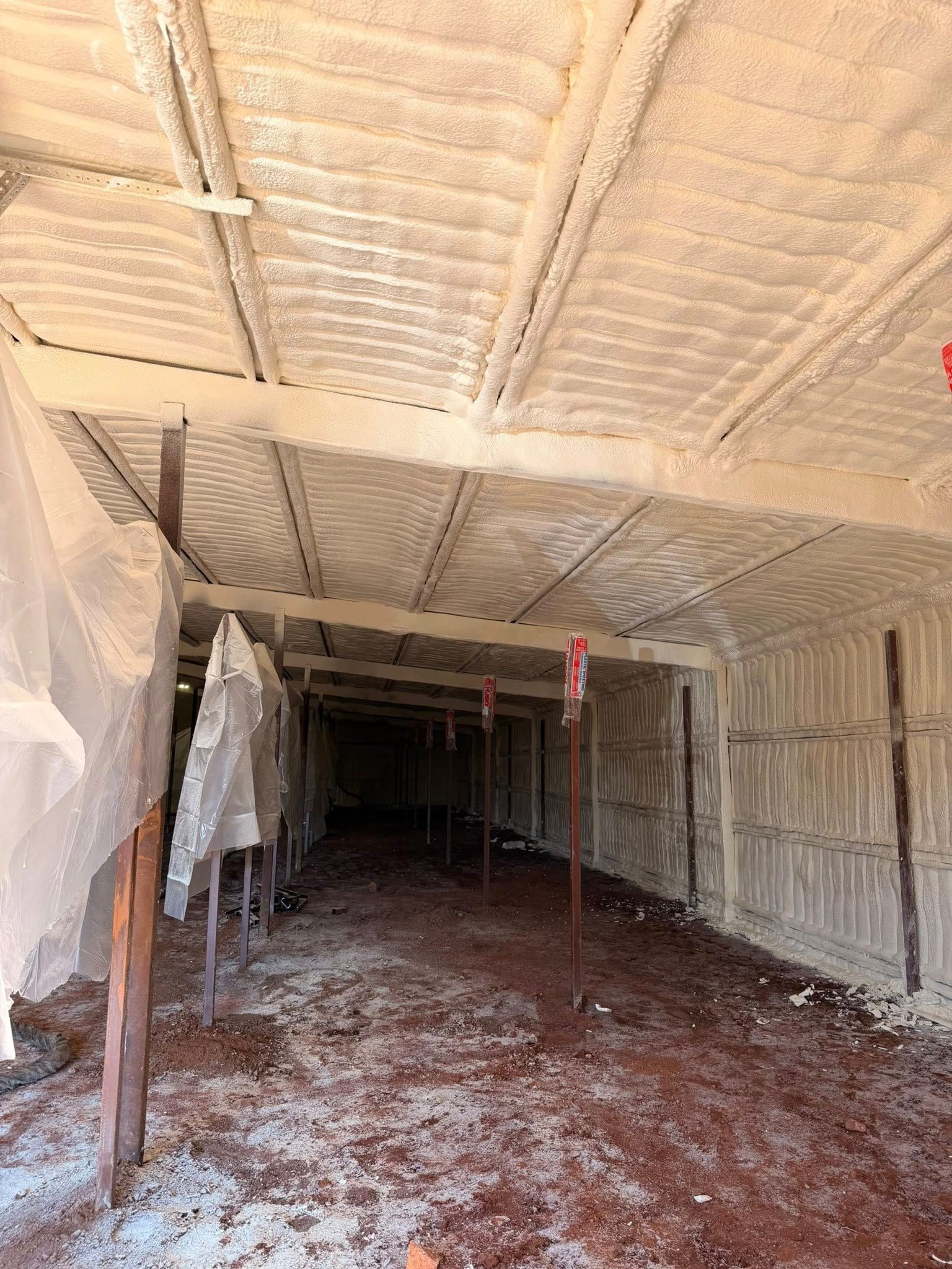 Partially finished room with exposed insulation, hanging plastic sheeting, and a dirt floor during construction