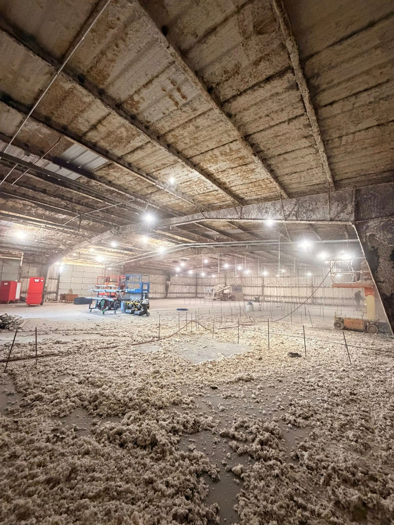 Dusty warehouse interior with a blue forklift and red equipment under bright overhead lights