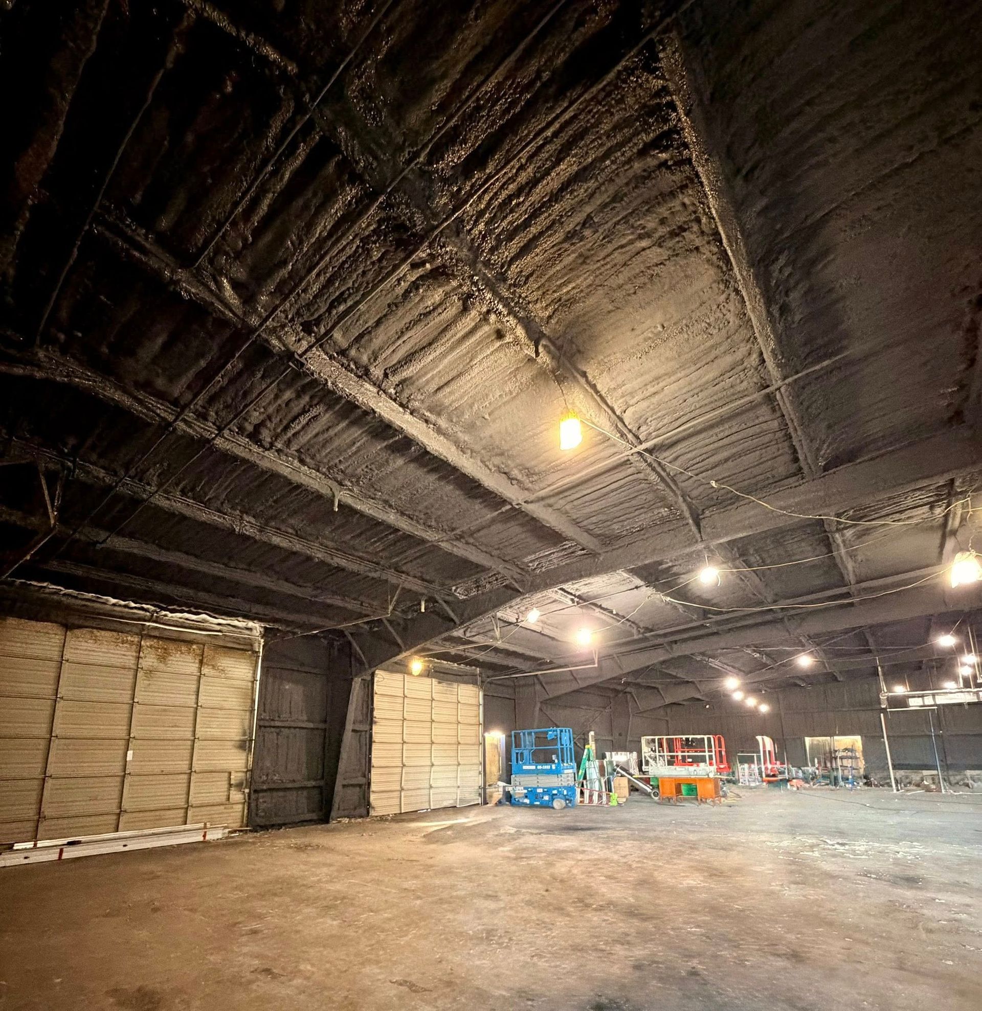Empty industrial warehouse with a dark ceiling, concrete floor, and stacks of pallets along the walls