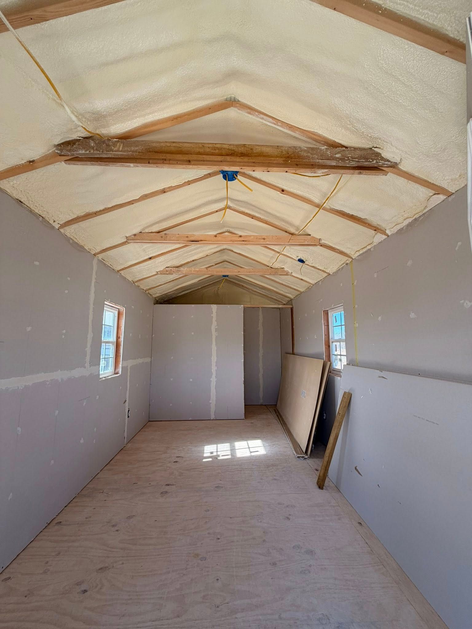 Empty unfinished room with gray walls, sloped insulated ceiling, and sunlight through small windows