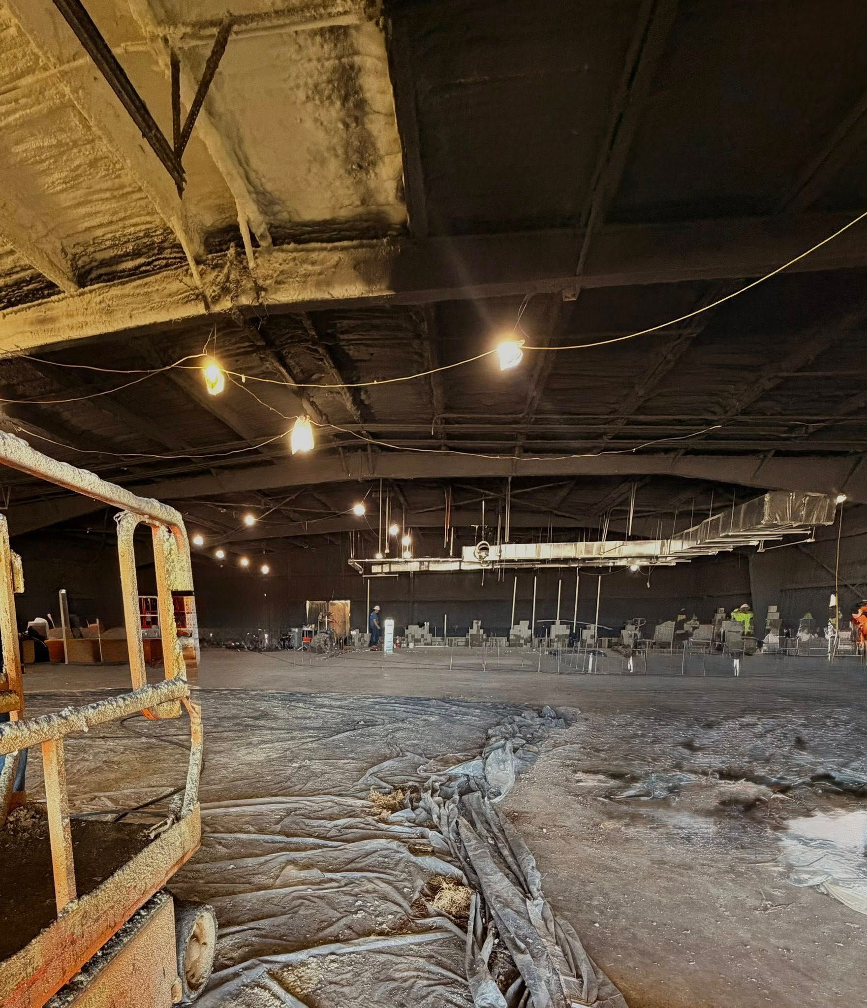 Damaged warehouse interior with rubble-strewn floor, exposed ceiling, and scattered lights