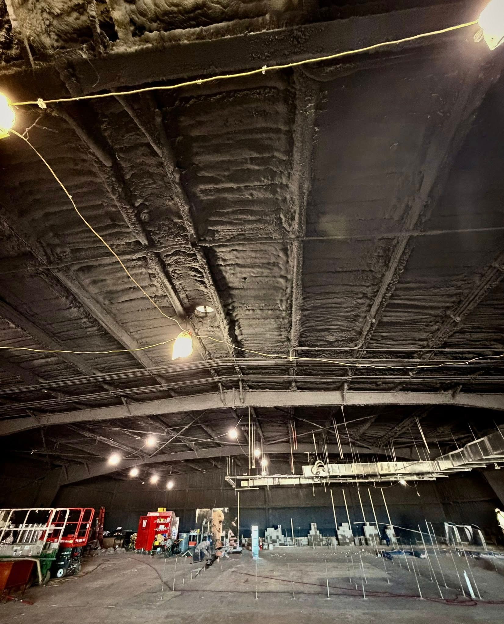 Dim warehouse interior with a black ceiling, hanging lights, and stacked equipment along the back wall.