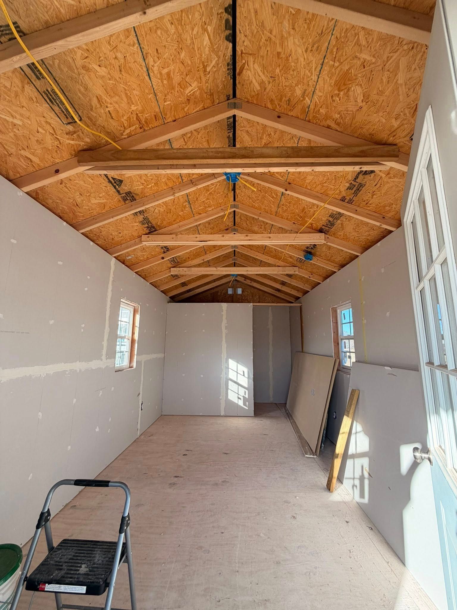 Long unfinished hallway with OSB ceiling, white drywall, and construction tools on the floor.