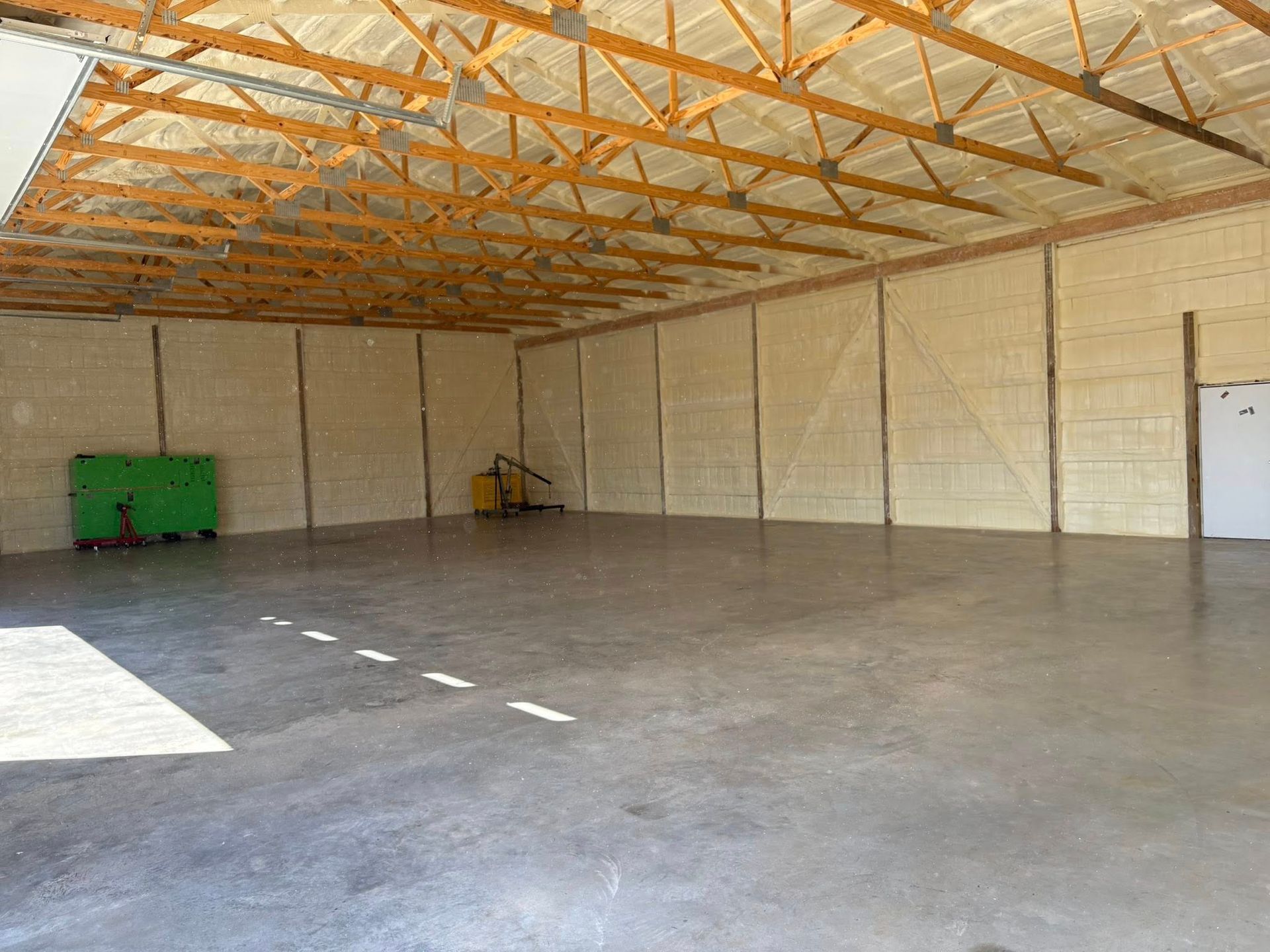 Empty warehouse with concrete floor, wood truss ceiling, tan walls, and a green utility cart in the corner