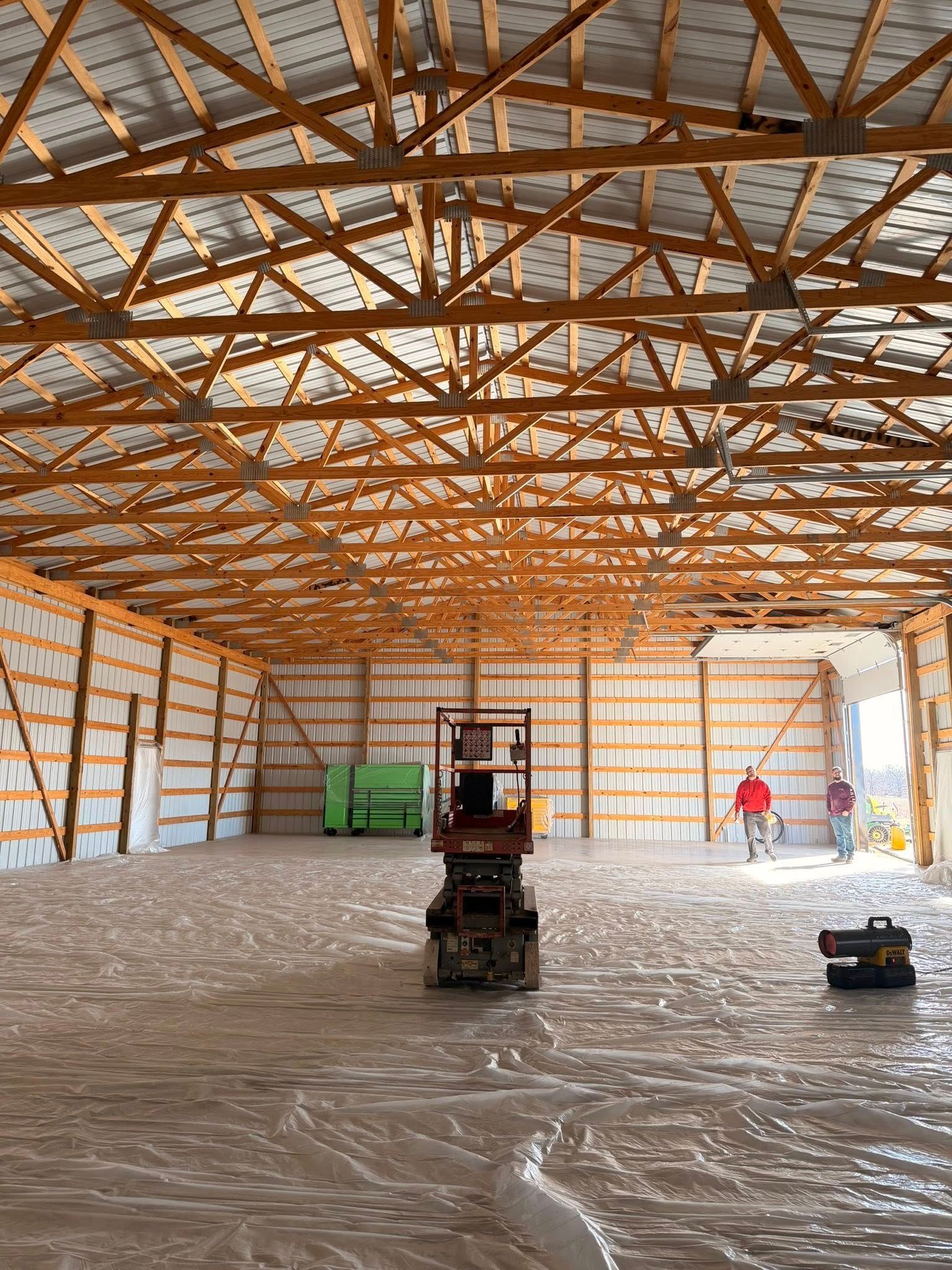 Inside a large metal-framed warehouse, a forklift sits on a plastic-covered floor during construction.
