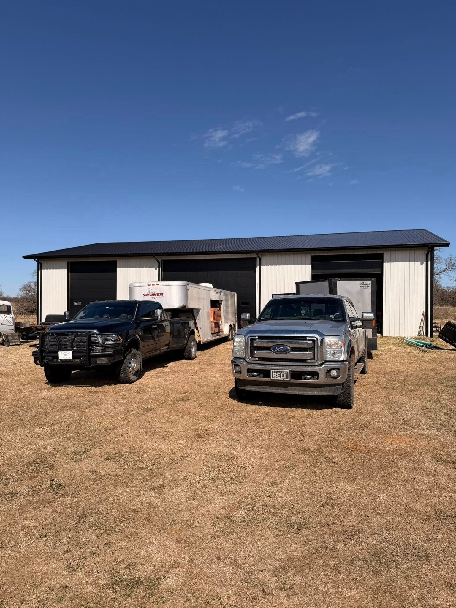 Two pickup trucks parked on a gravel lot in front of a metal building under a blue sky