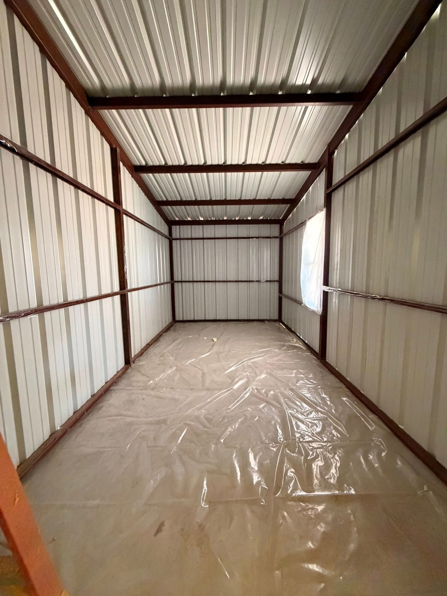 Empty corrugated metal shed with a plastic-covered floor and exposed steel beams.