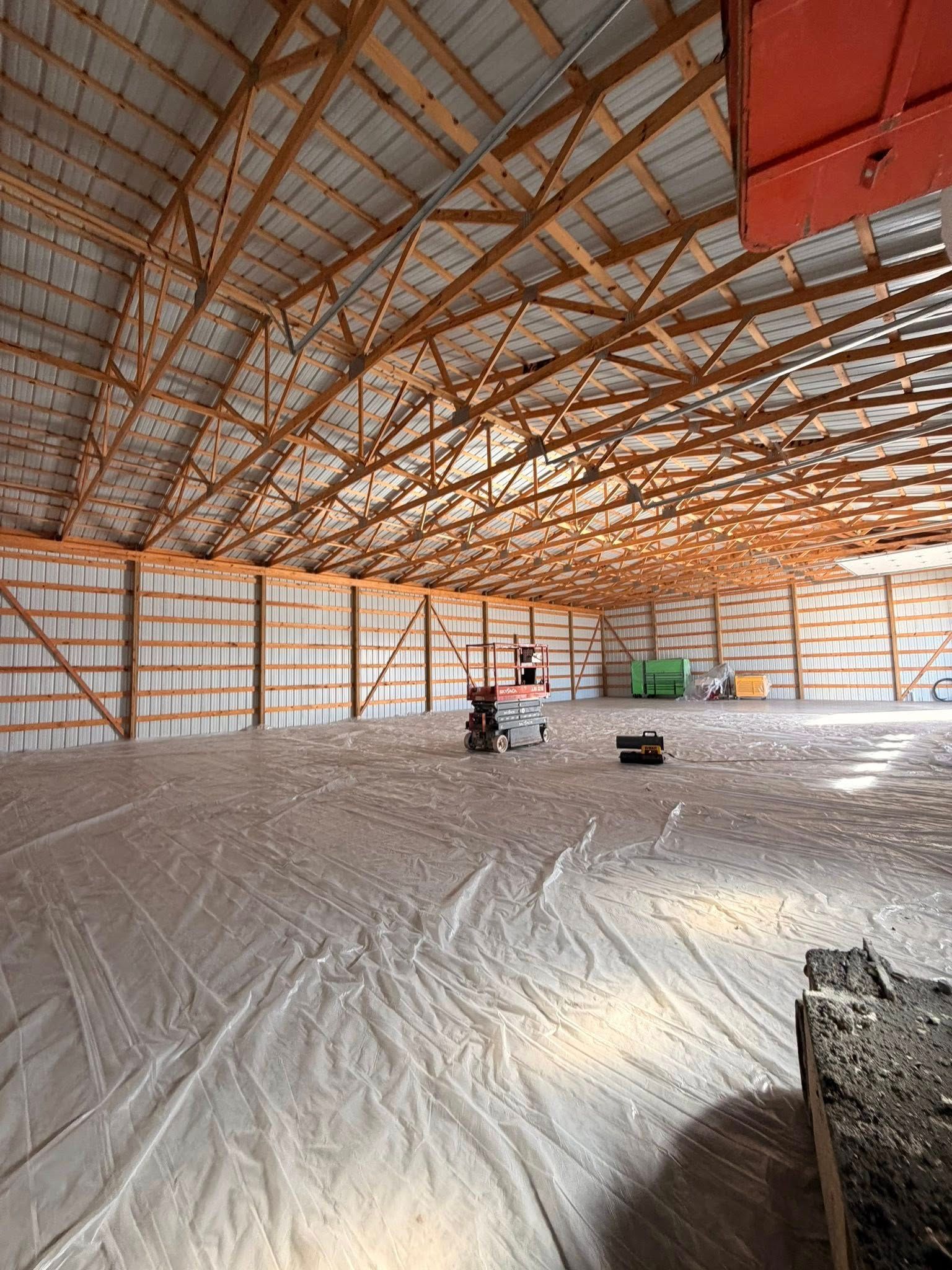 Large empty warehouse interior with a high wooden truss roof and a few workers on the concrete floor.