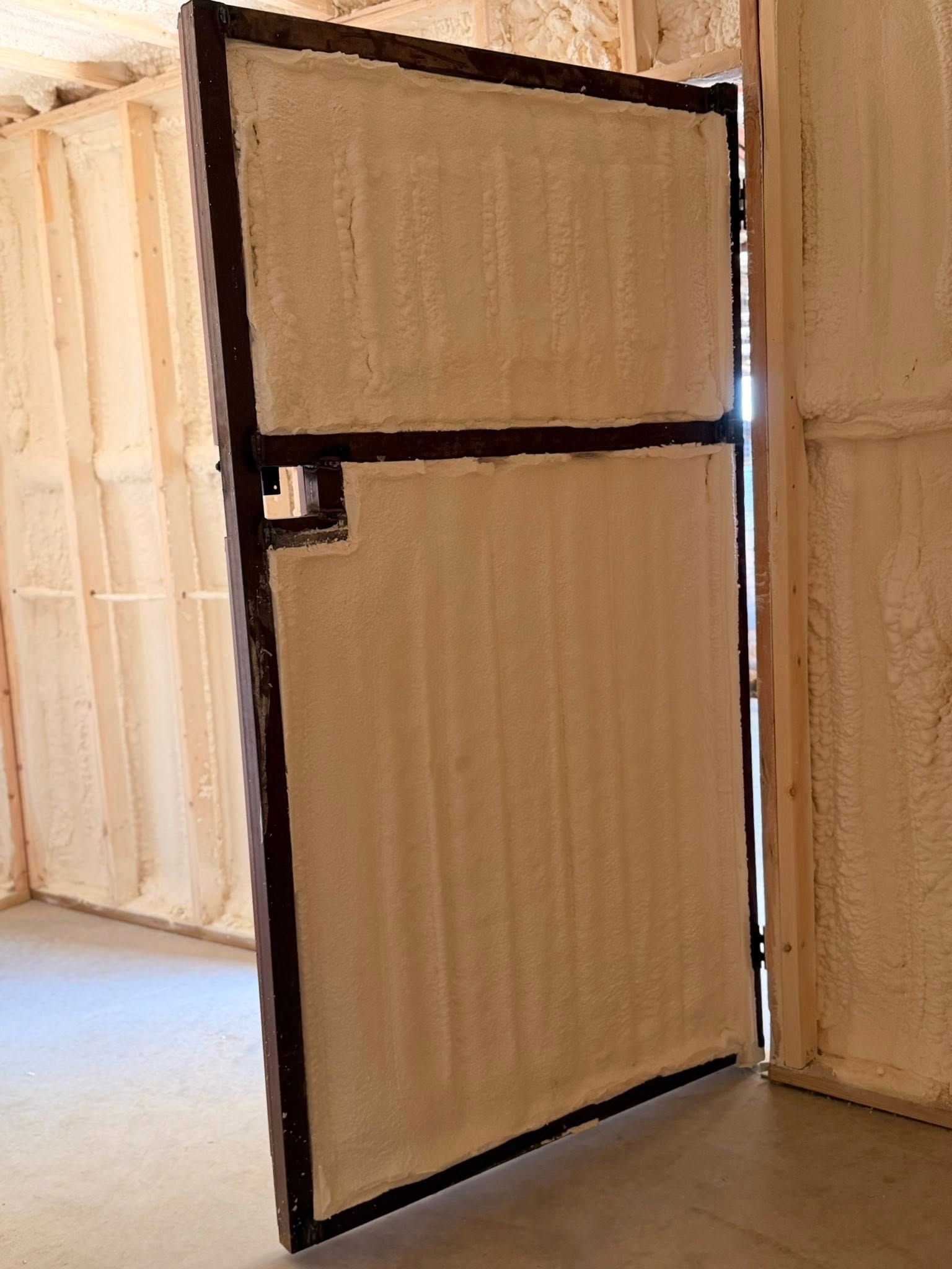Open wooden door with black frame in a partially framed interior wall.