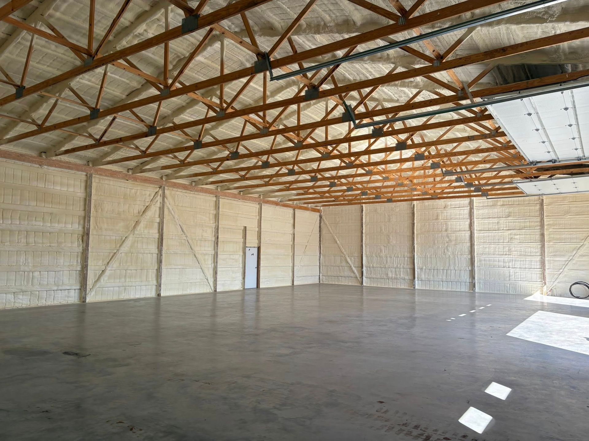 Empty warehouse interior with exposed wooden trusses, concrete floor, and white walls