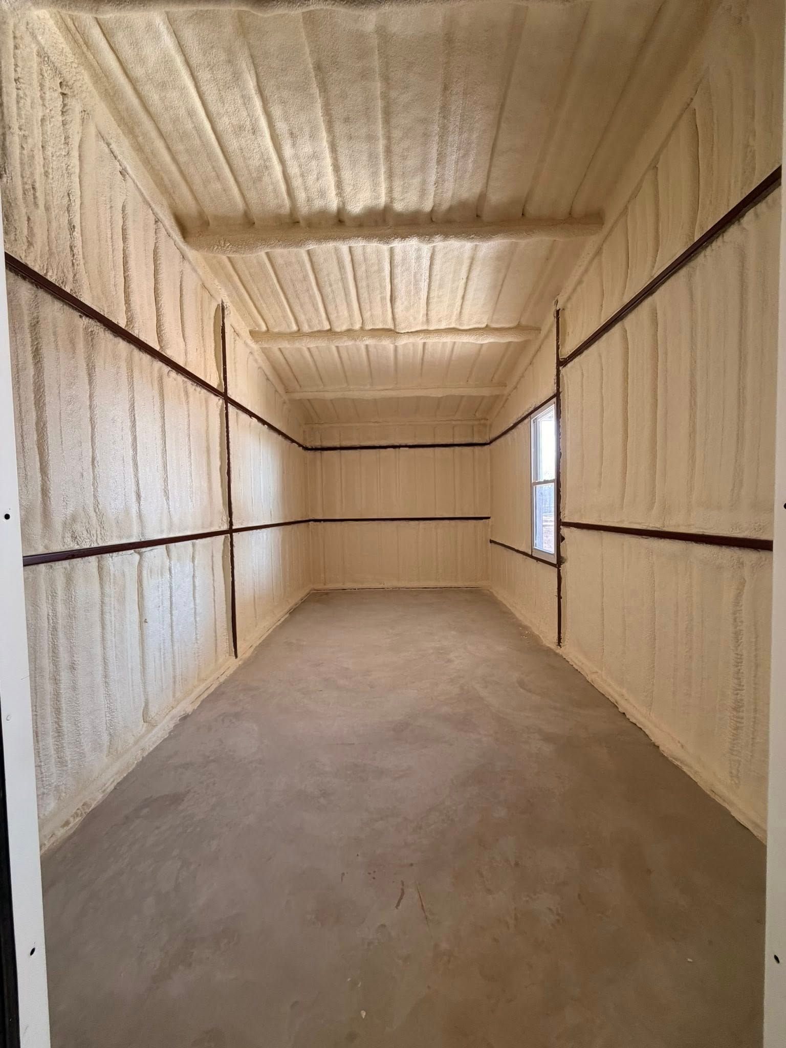 Empty unfinished room with white insulated walls, exposed seams, and a single window.