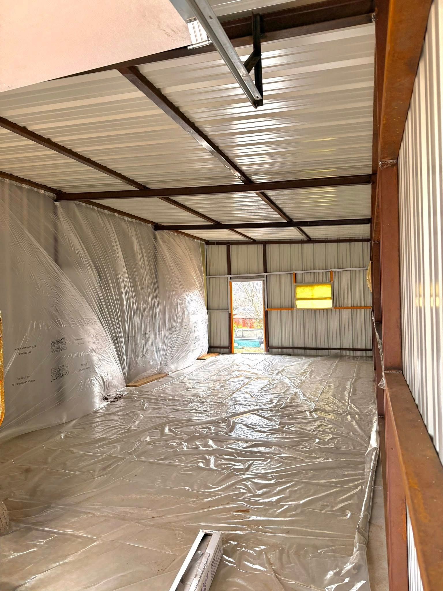 Empty metal shed interior lined with reflective insulation and plastic sheeting on the floor