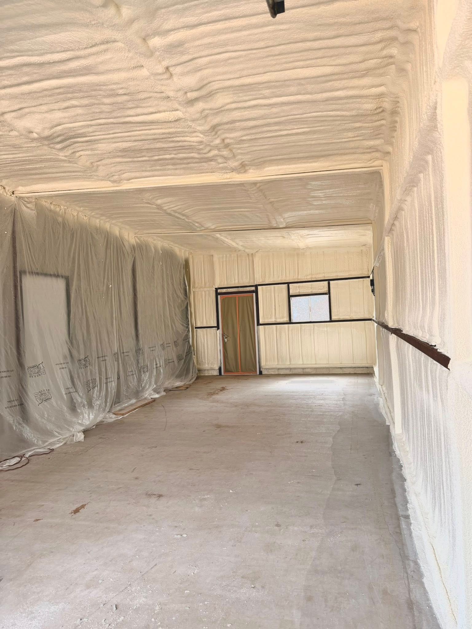 Empty unfinished room with white walls, concrete floor, and a small window and door at the back.