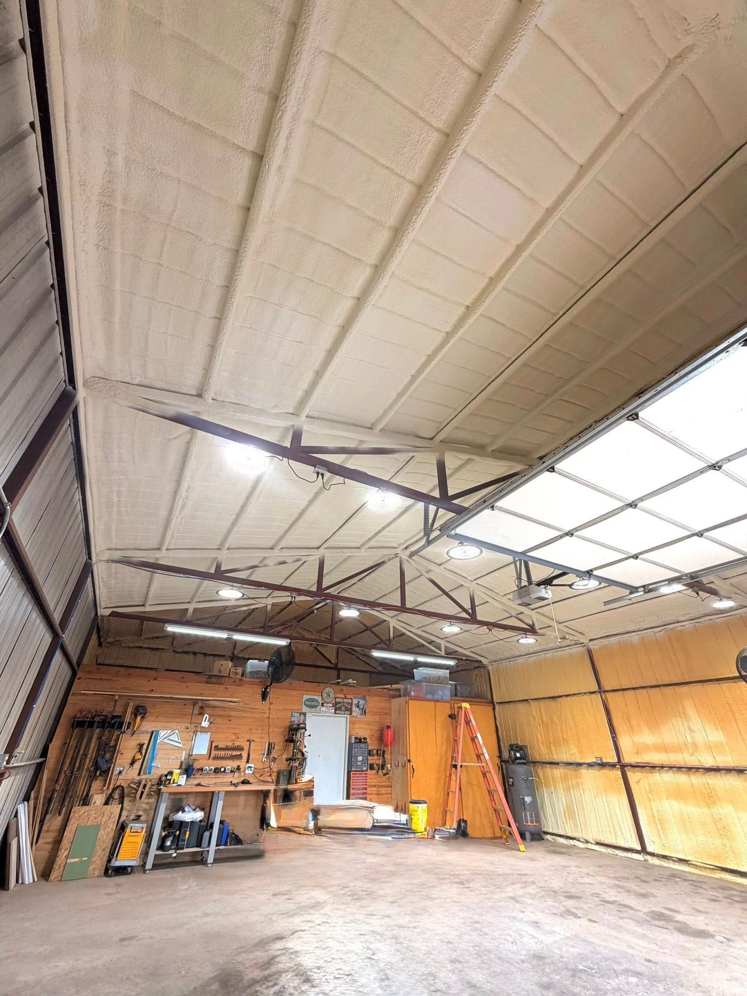 Sparse workshop interior with high ceiling, scattered tools, shelves, and a large open garage door