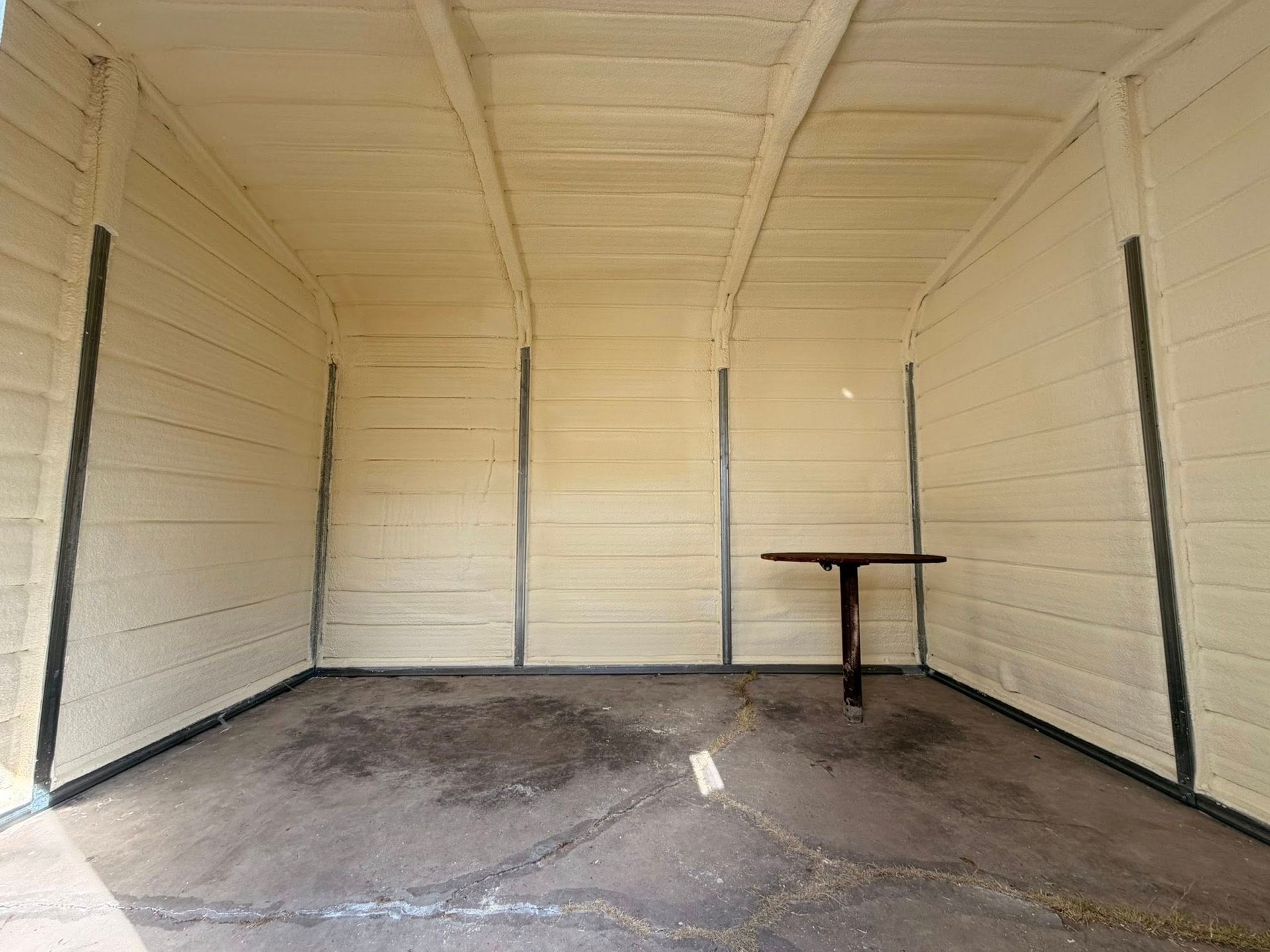 Empty beige shed interior with a concrete floor and a small table against the right wall