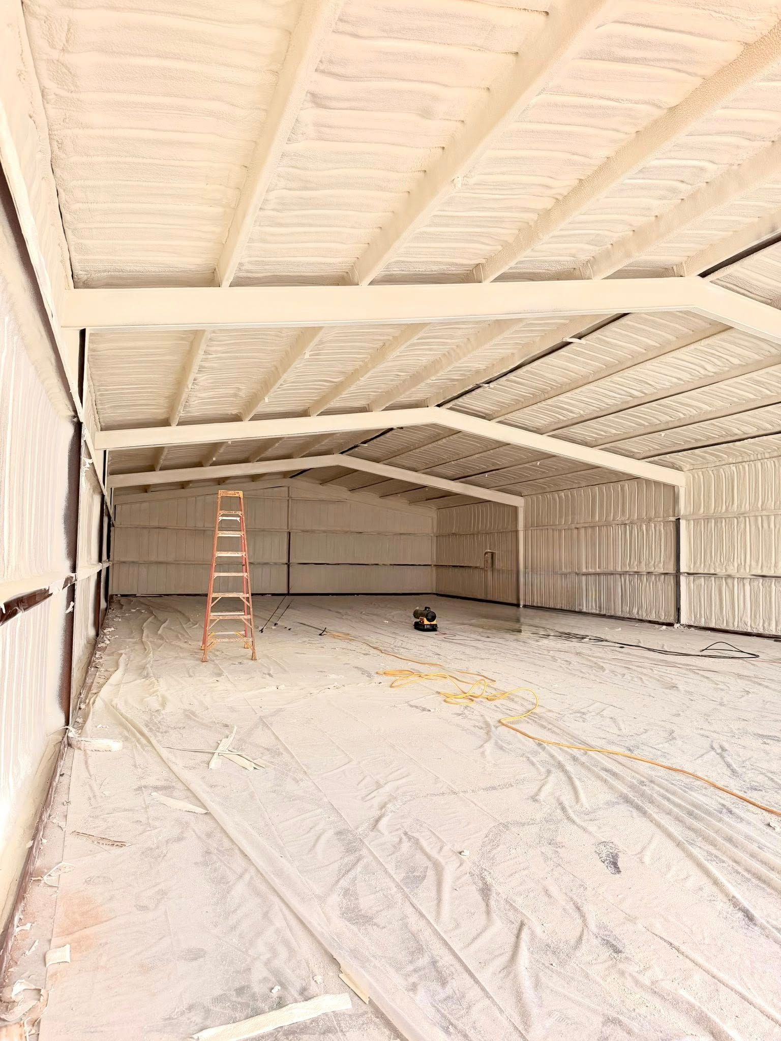 Empty white metal workshop with exposed beams, a ladder, and a dusty floor under construction