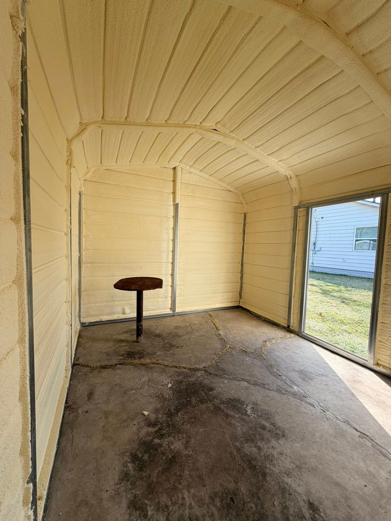 Empty beige enclosed porch with a small table and open doorway to the outside.