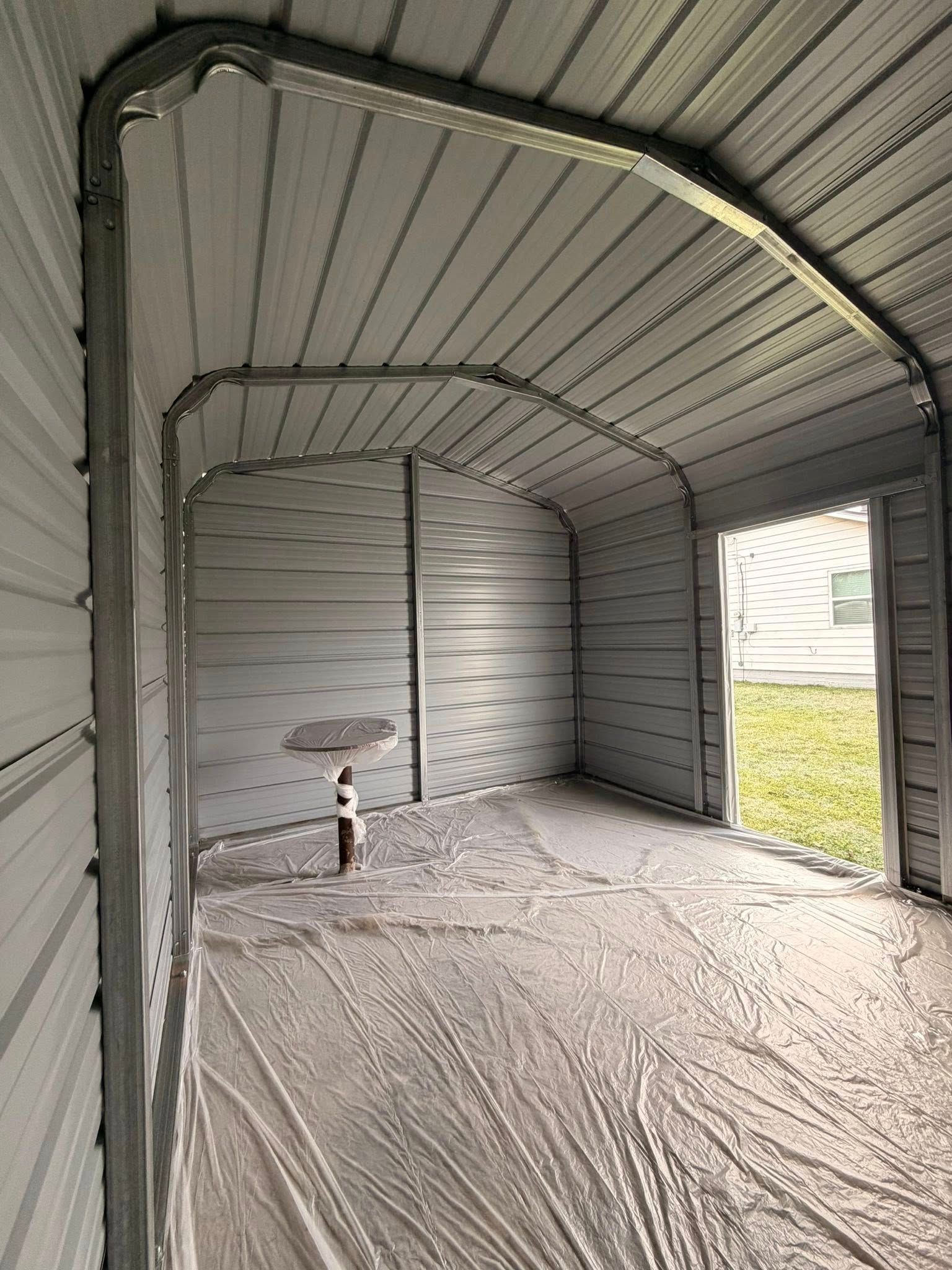 Empty metal shed interior with corrugated walls, arched roof, and open doorway showing grass outside