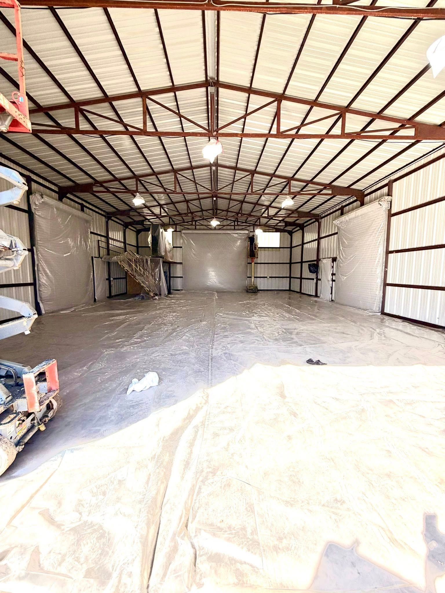 Empty industrial warehouse interior with metal roof beams, concrete floor, and a small forklift at left