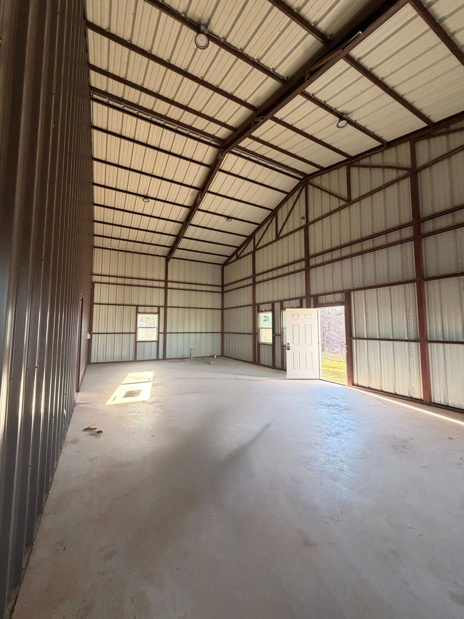 Empty metal warehouse interior with high roof, concrete floor, and sunlight through open doorways.