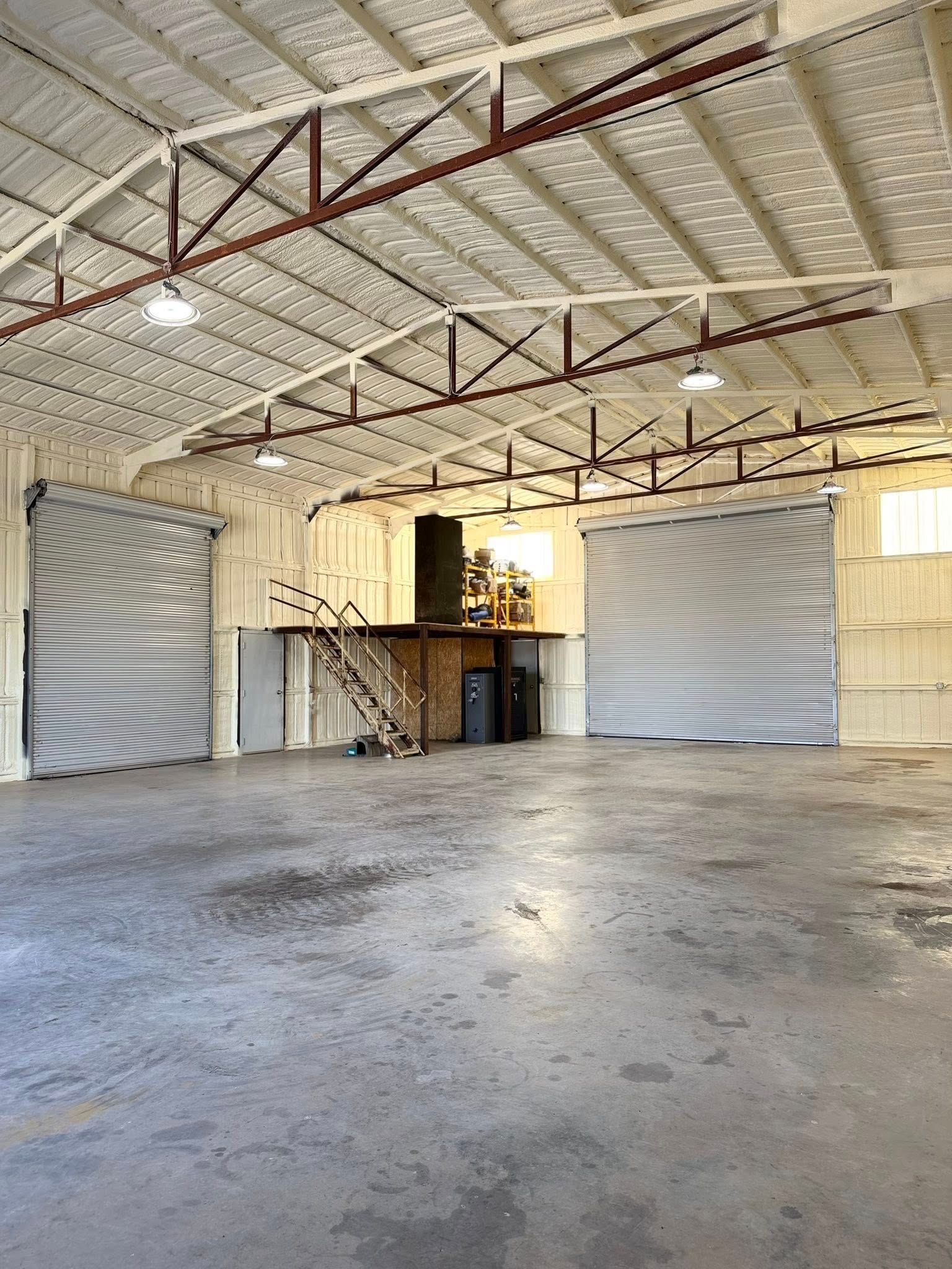 Empty warehouse interior with concrete floor, exposed trusses, and large roll-up doors.