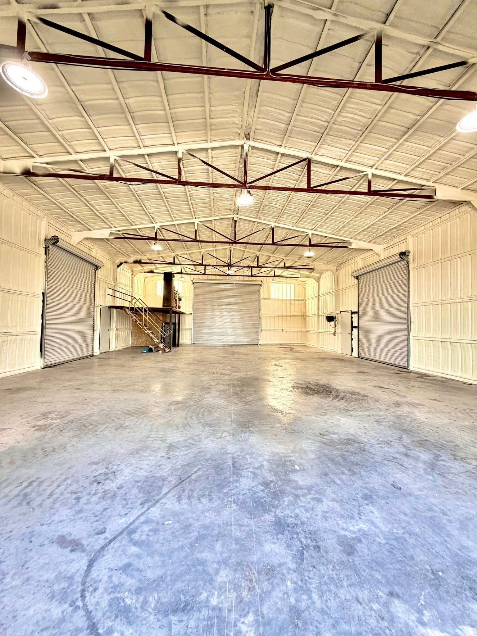 Empty industrial warehouse interior with white walls, exposed rafters, and a concrete floor