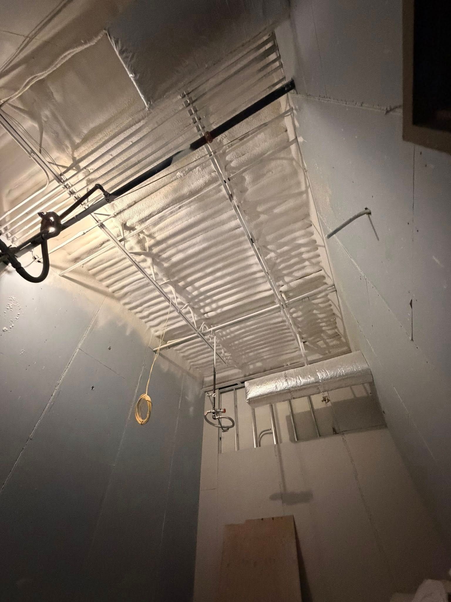 Ceiling view of a room under construction with exposed metal framing, wiring, and hanging lights