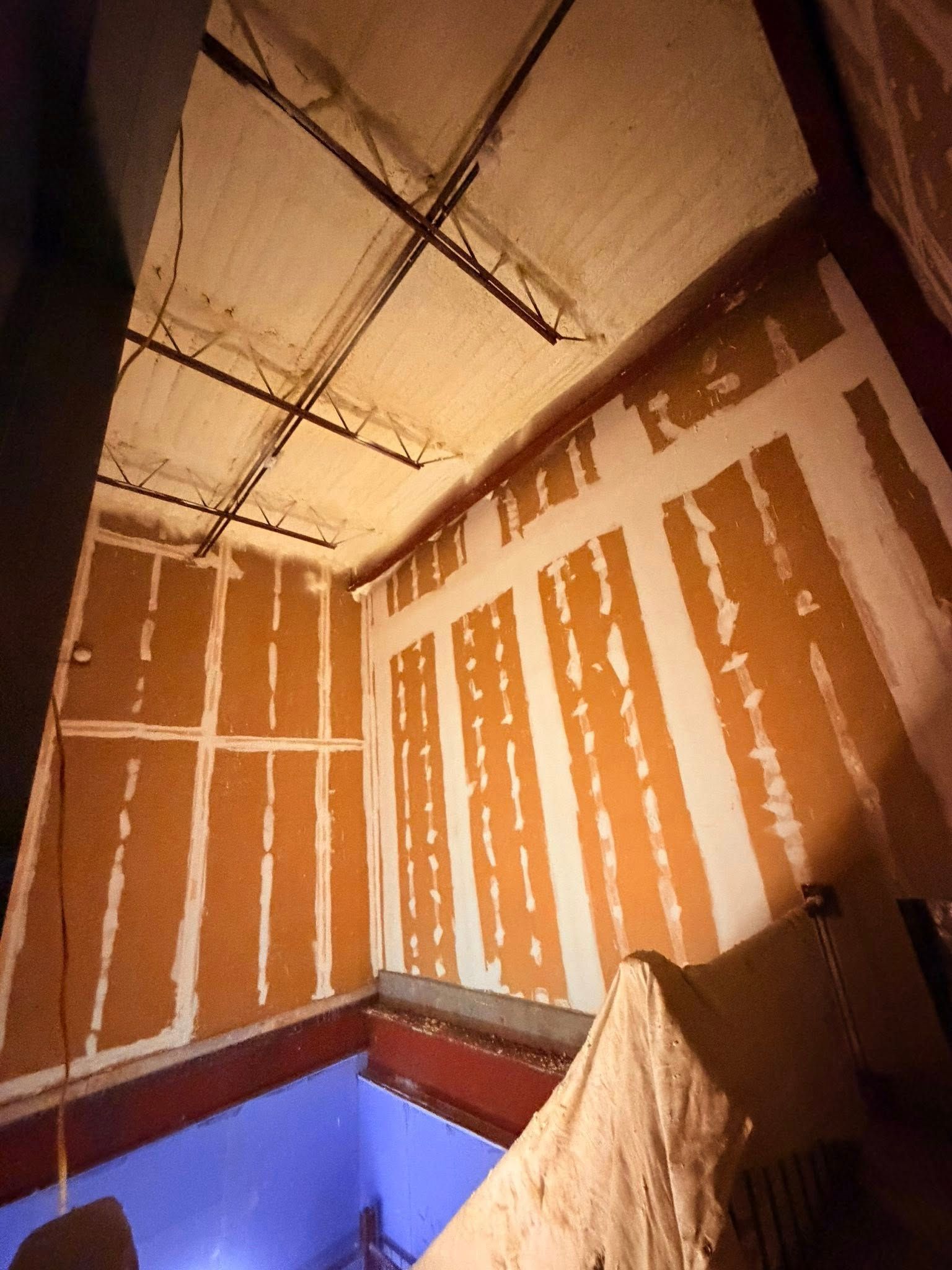 Unfinished stairwell with brown drywall, exposed ceiling, and a blue wall below