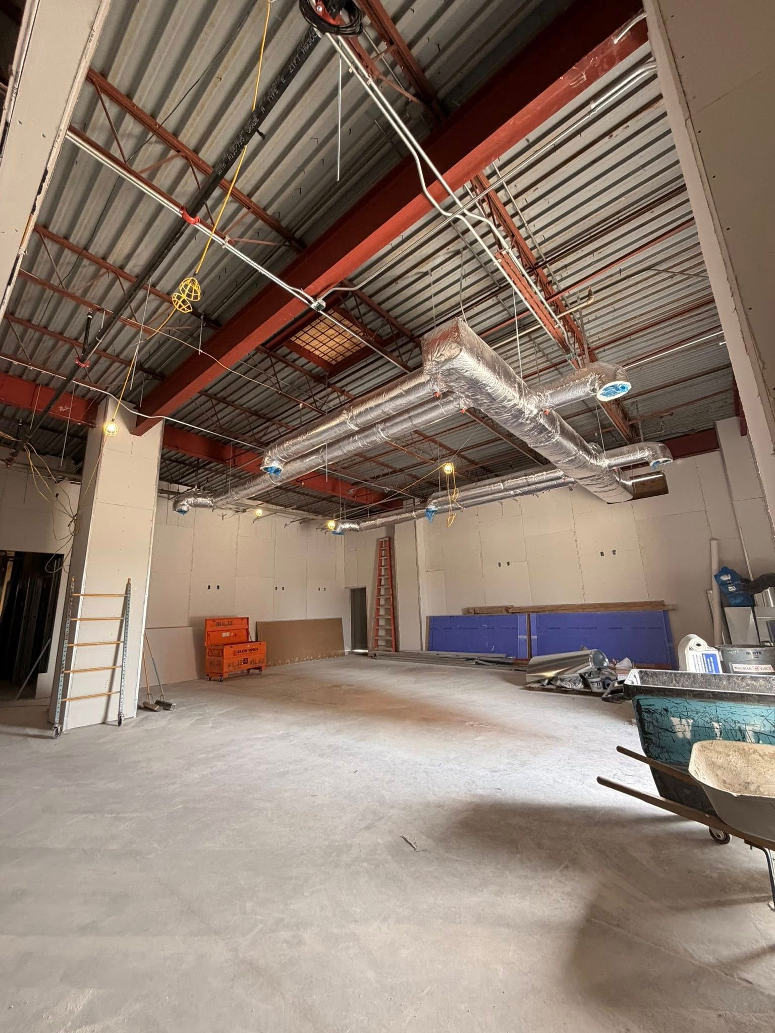 Empty industrial room with exposed ceiling beams, ladder, and scattered construction materials.