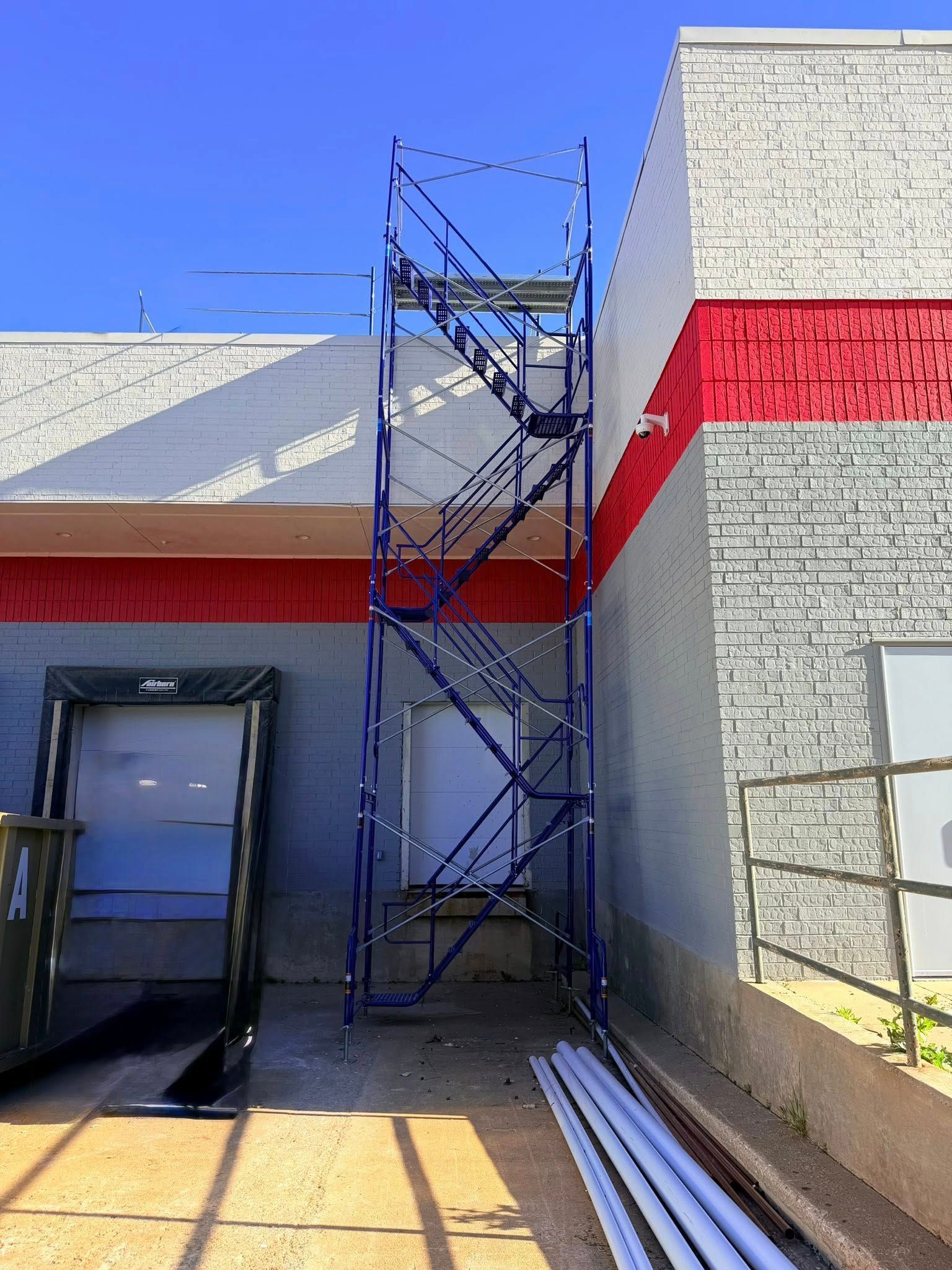 Scaffolding beside a white building with a red stripe under a blue sky