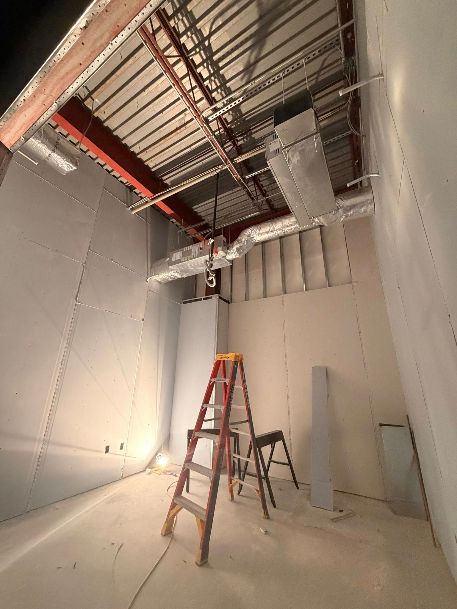 Partially finished room with drywall, exposed ceiling ducts, and a red ladder on the floor