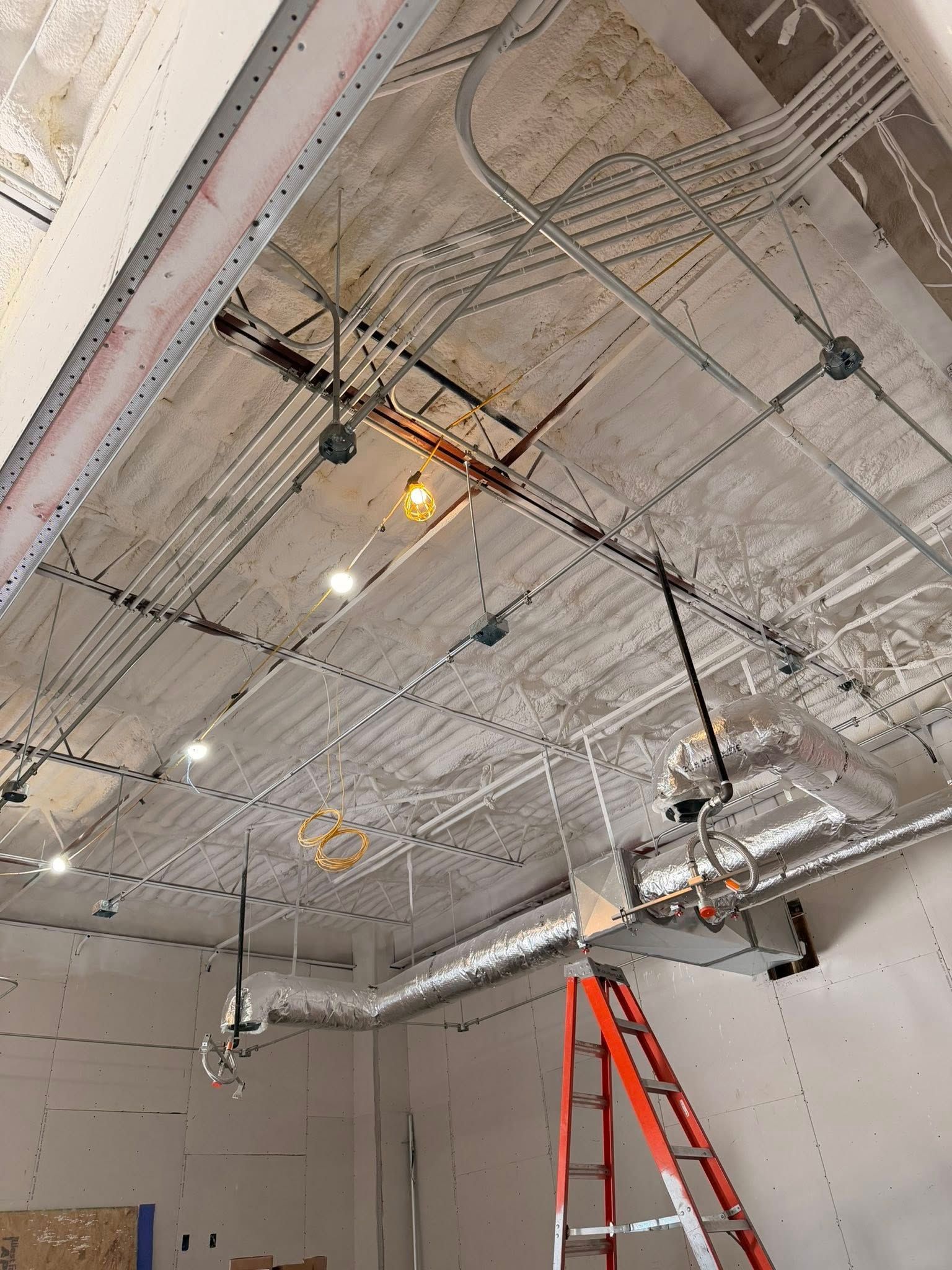 Ceiling utility work area with exposed ducts, wiring, hanging lights, and a red ladder