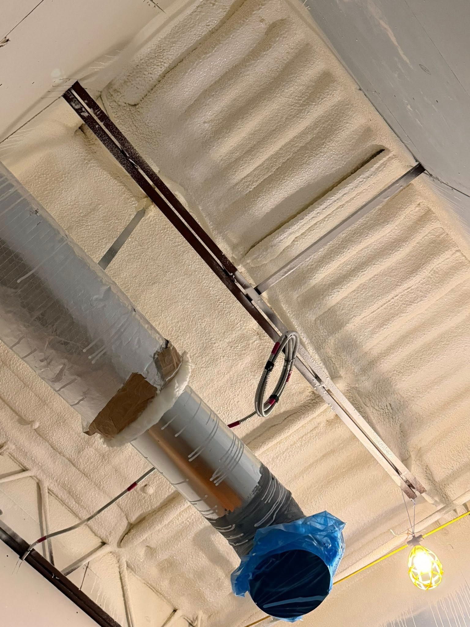 Ceiling with exposed silver ductwork, blue vent, and a lit bulb in an industrial space