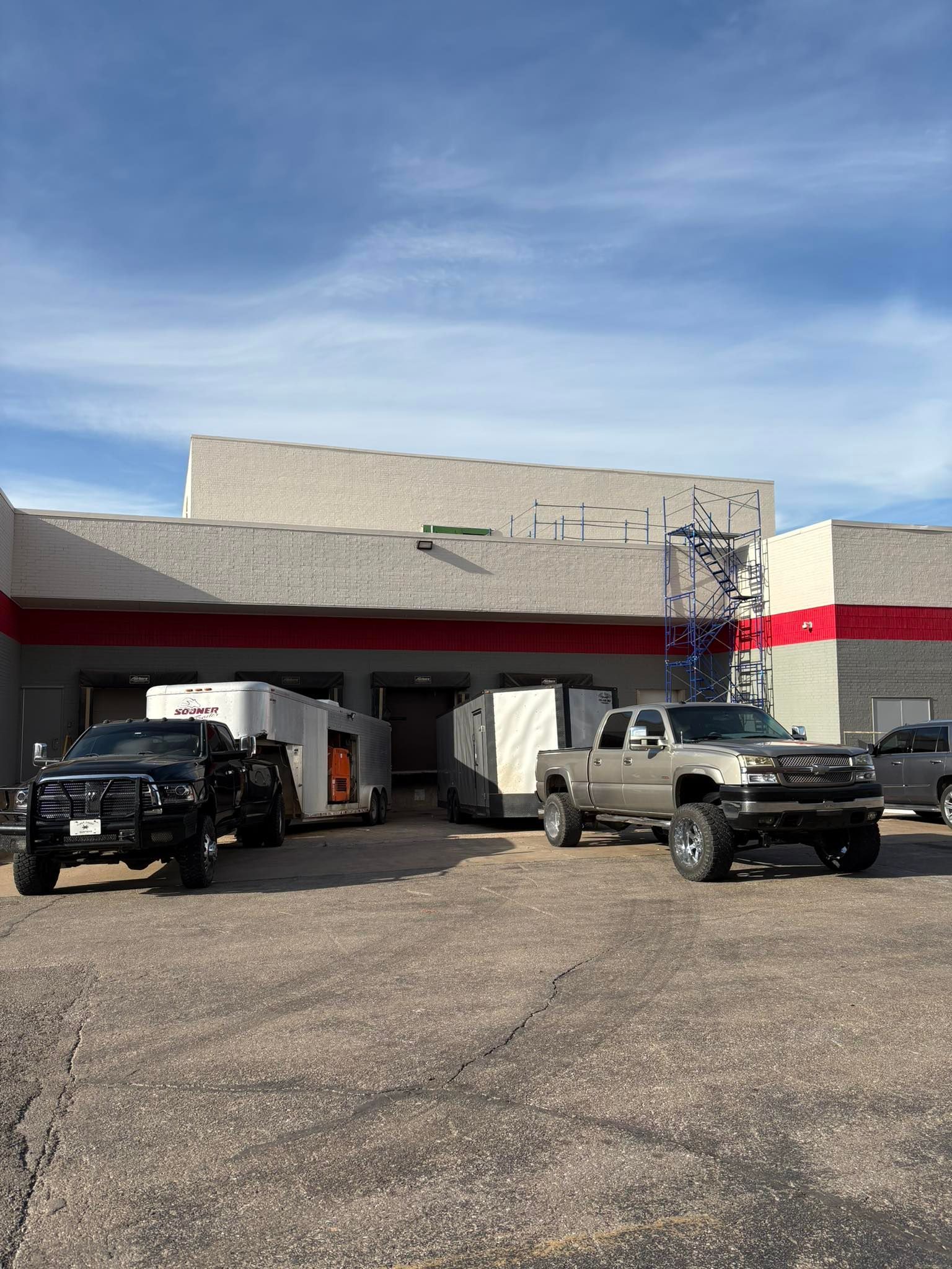 Two trucks parked outside a building under repair with scaffolding and a red stripe.